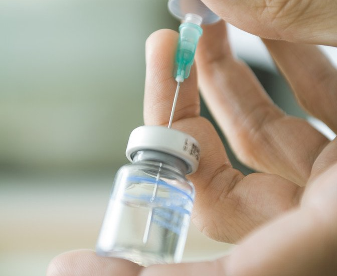 A vaccine bottle with a needle being pushed into the top.