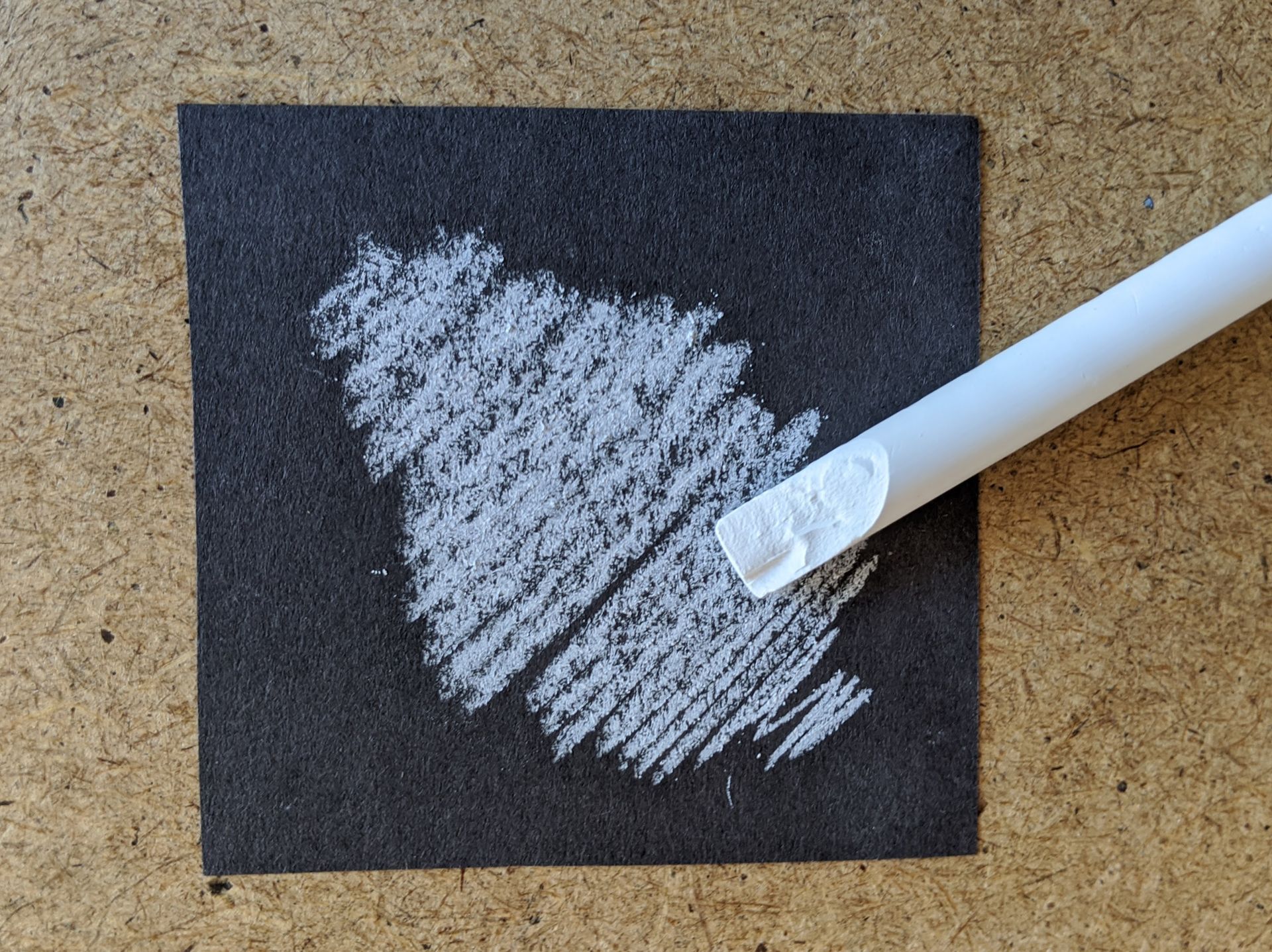 A dark coloured piece of paper with chalk scribble on it.