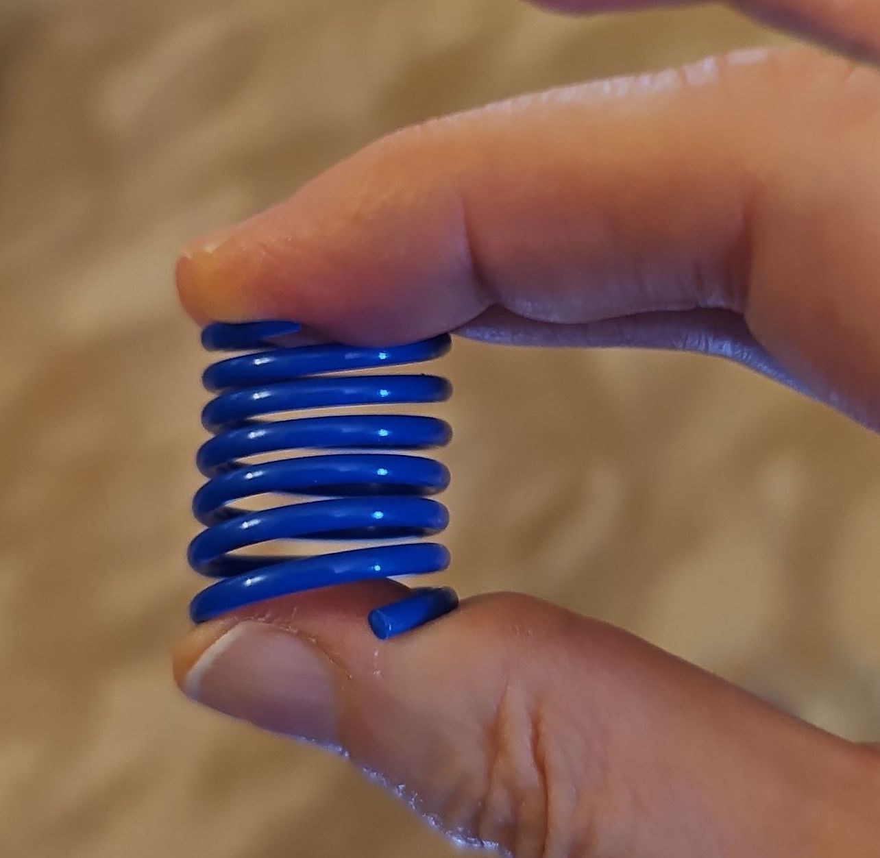 A colourful large spring. It's being held tightly between the thumb and forefinger.