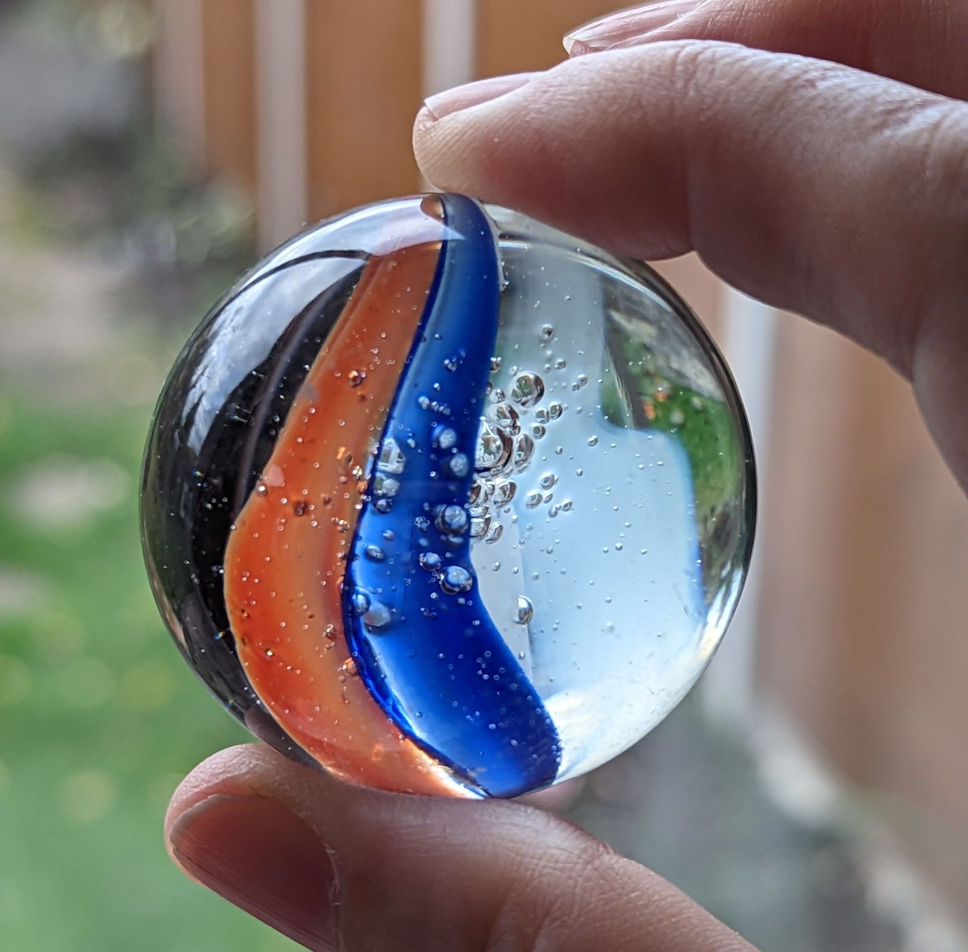 A giant marble with a two tone ribbon running through it. Someone is holding it between their thumb and forefinger
