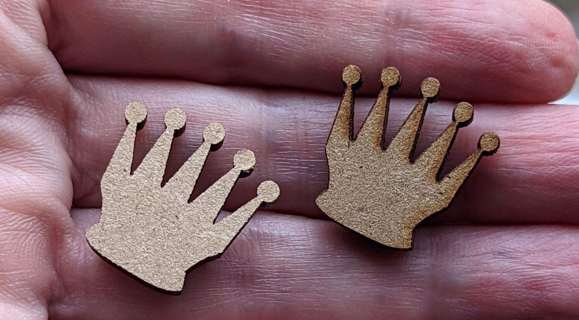Two small wooden cutout crowns on a person's hand.