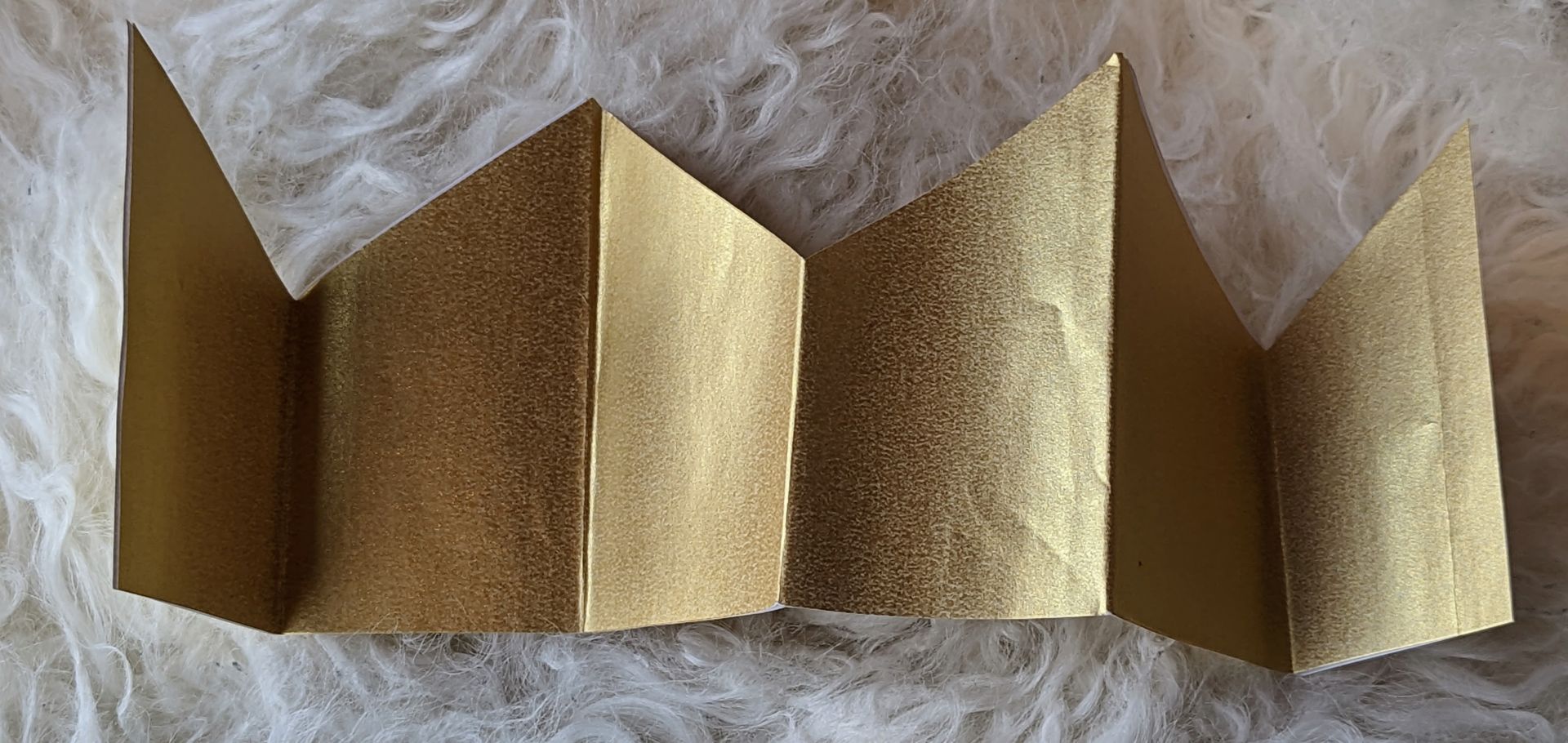 A gold paper crown sitting on a furry cushion.