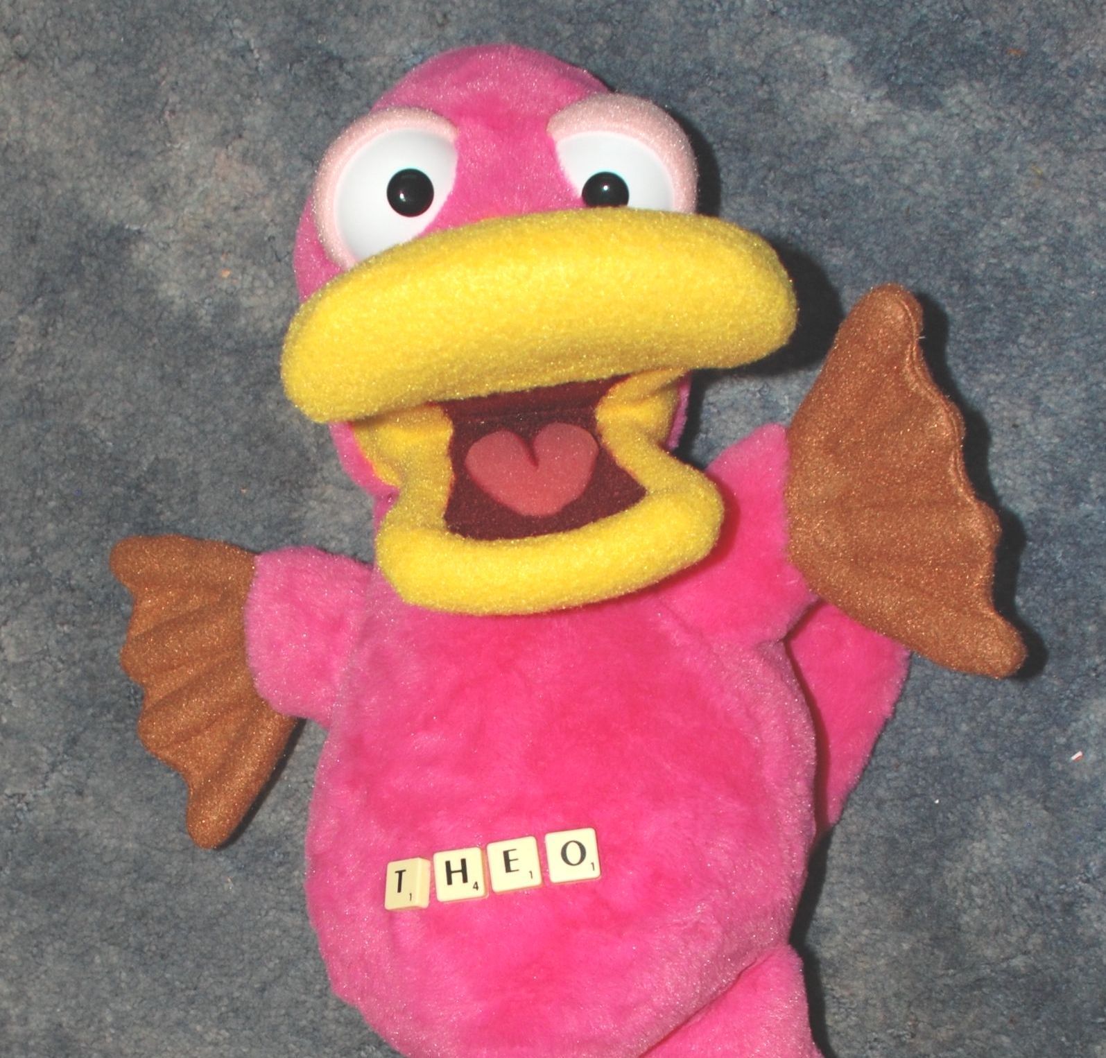 Theo the pink platypus puppet with scrabble letters on his Tummy. They spell his name.