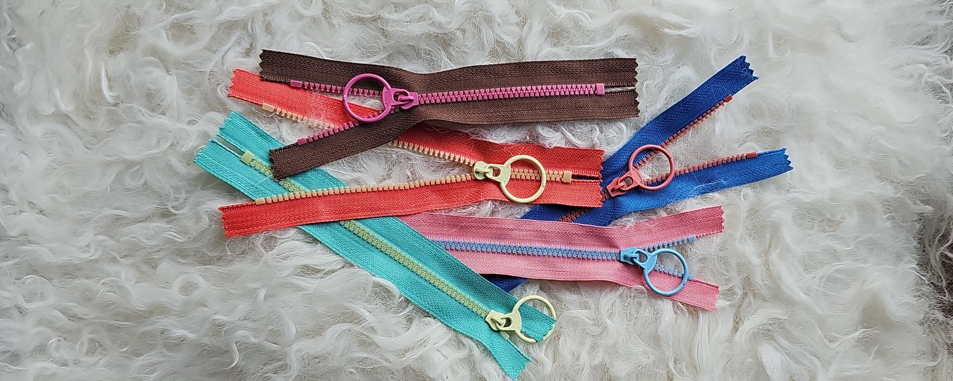 Lots of colourful zips placed on a fluffy cushion.