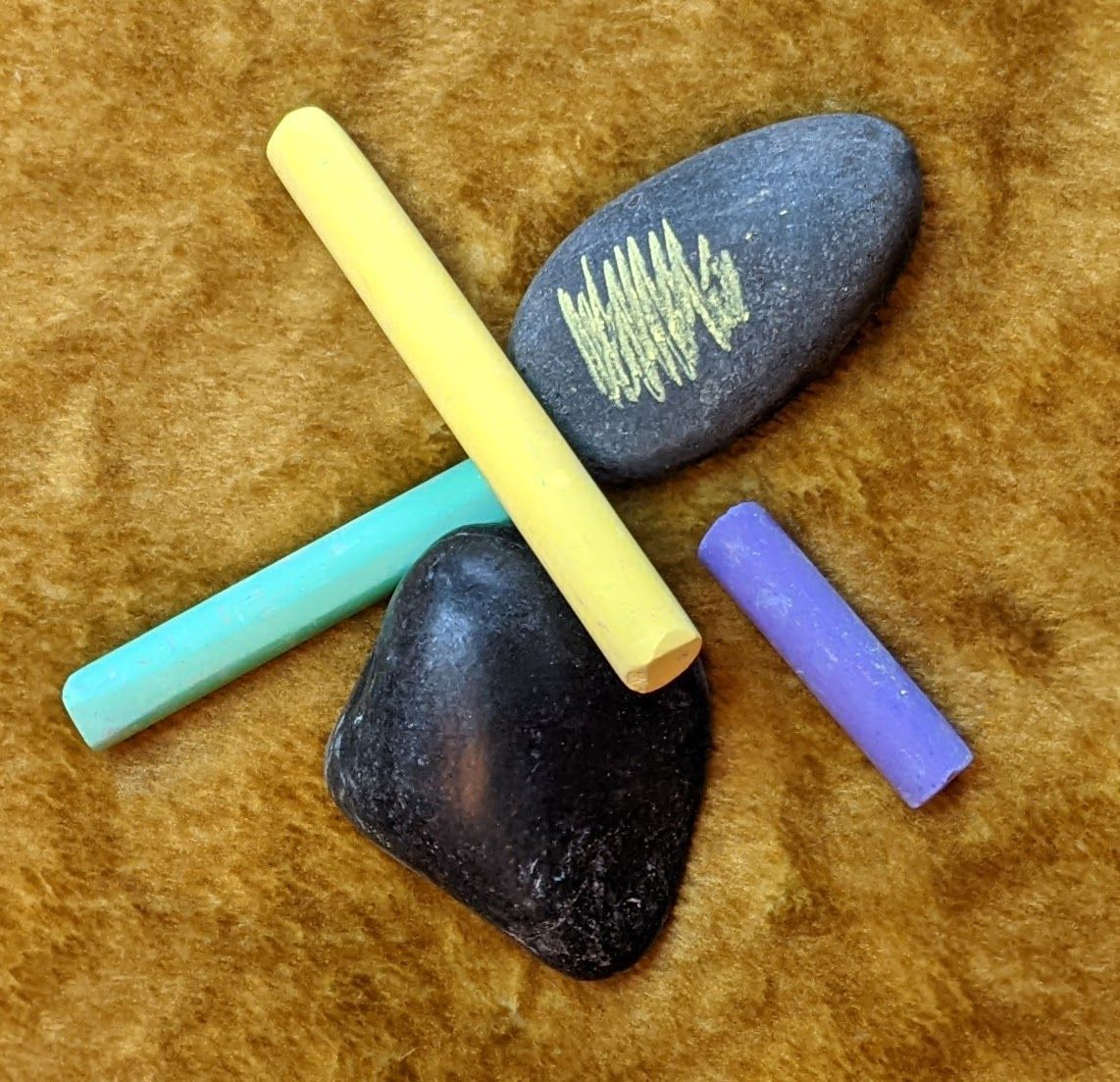 Two stones and three sticks of chalk. One of the stones has a yellow scribble on it.
