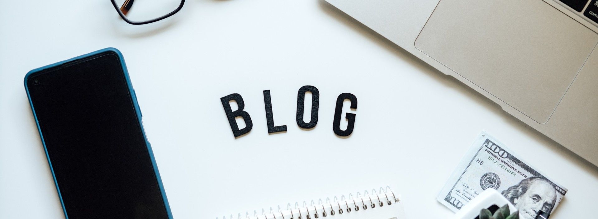 Blog Schriftzug auf dem Tisch umgeben von Laptop, Notizbuch und Brille