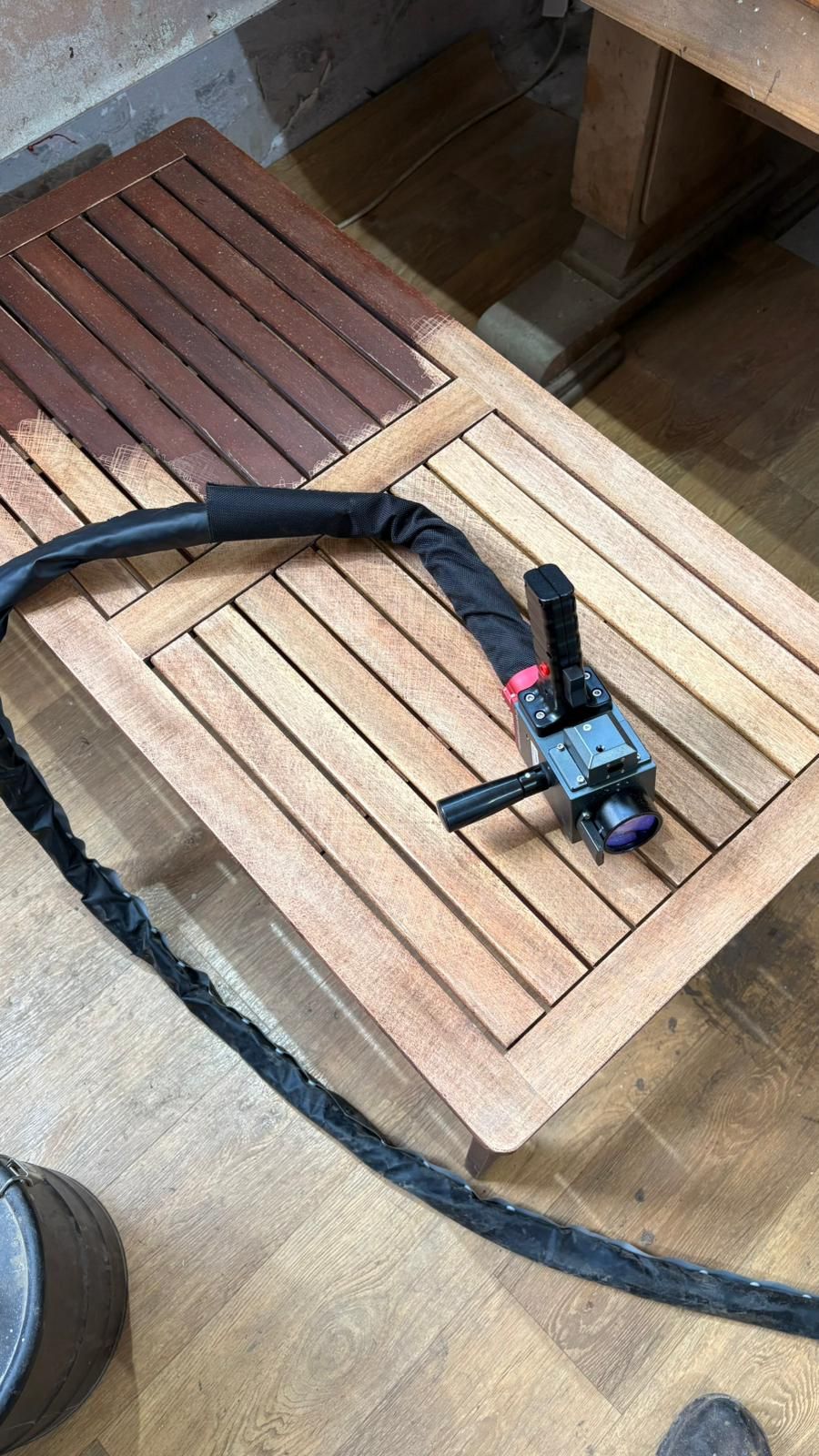 Tête de laser posée sur table en bois partiellement décapée, illustration du décapage laser propre e