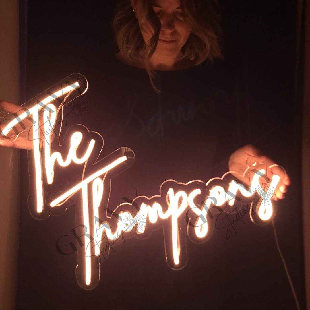 owner Jenna Musgrave holding a custom neon wedding sign that says the Thompsons