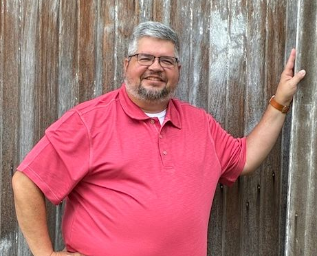 Kyle Hoffman in a red shirt, standing in front of a wooden wall