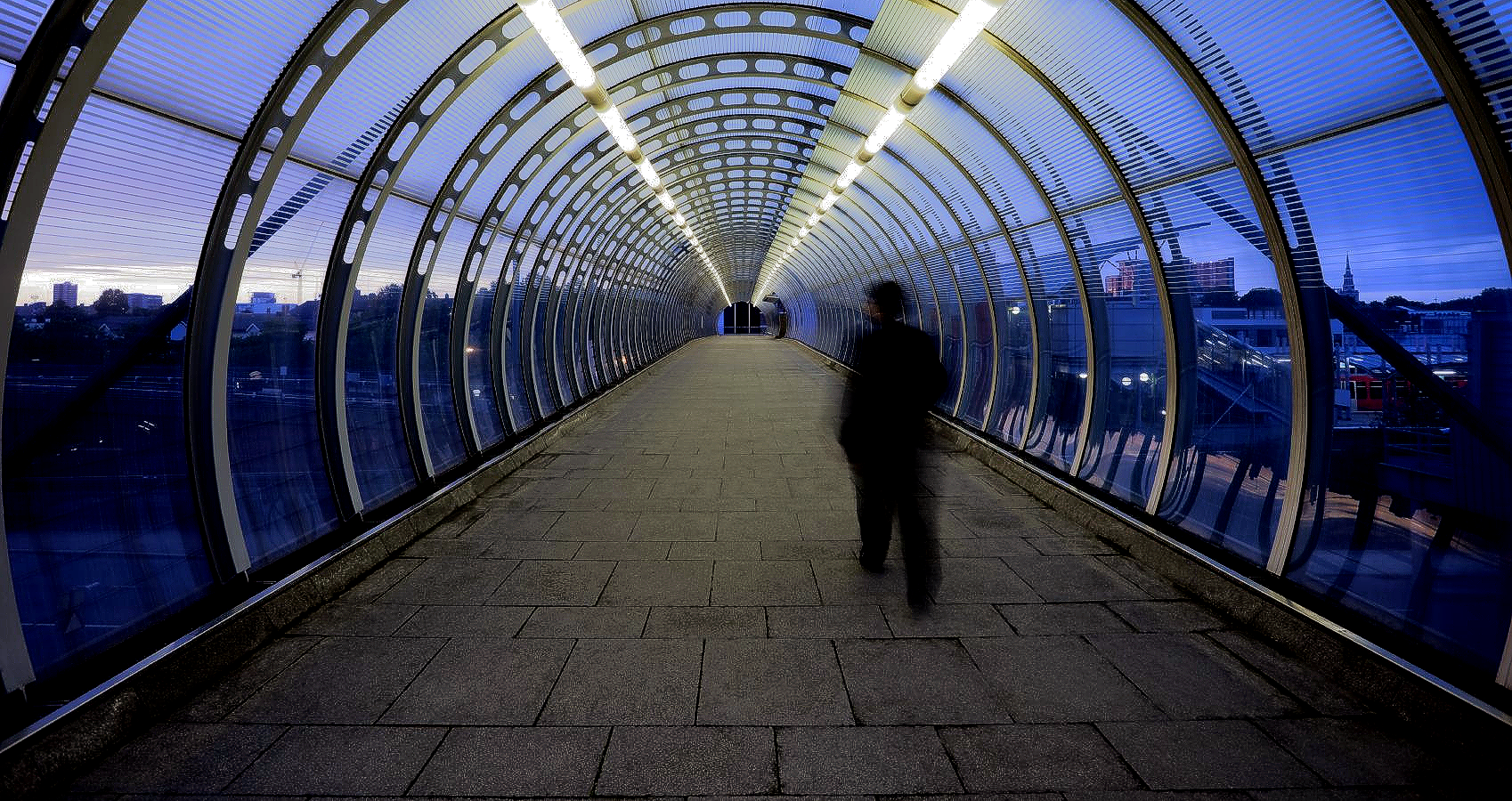 Ein Fußgänger läuft in der blauen Abend-Dämmerung durch einen Glastunnel. Bild aus der Fotoworkshop-Beschreibung Kreatives Sehen bei Fotokurs Nürnberg.