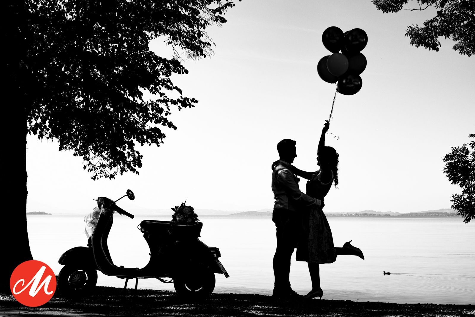 hochzeitspaar mit luftballons und vespa als silhouette vor chiemsee masters of wedding photography