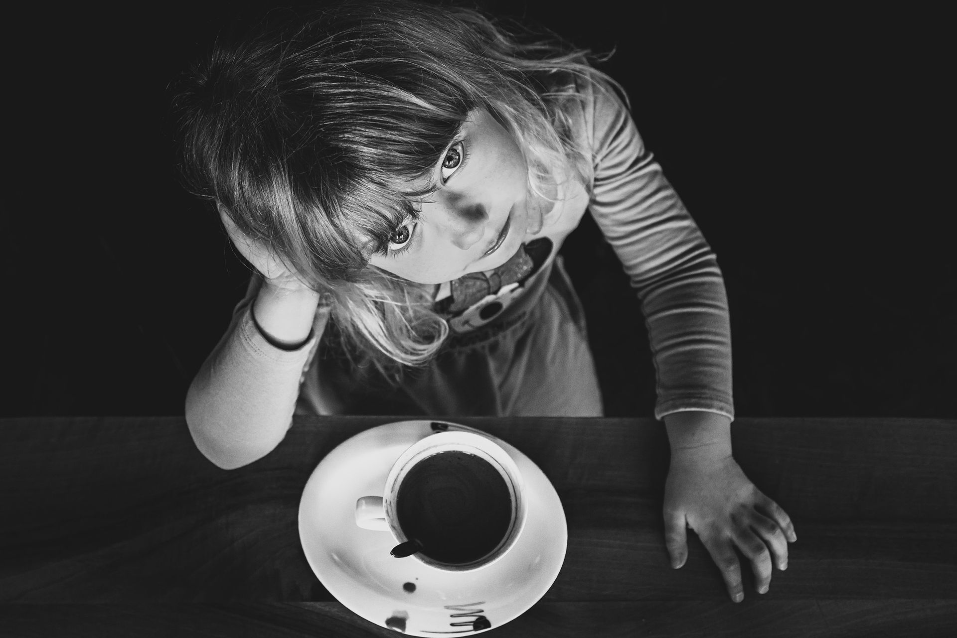 Authentisches Kinderportrait Fotograf Traunstein mädchen sitzt mit kakao am tisch stützt kopf auf hand familienportraits fotograf traunstein schwarz weiß kinderportrait