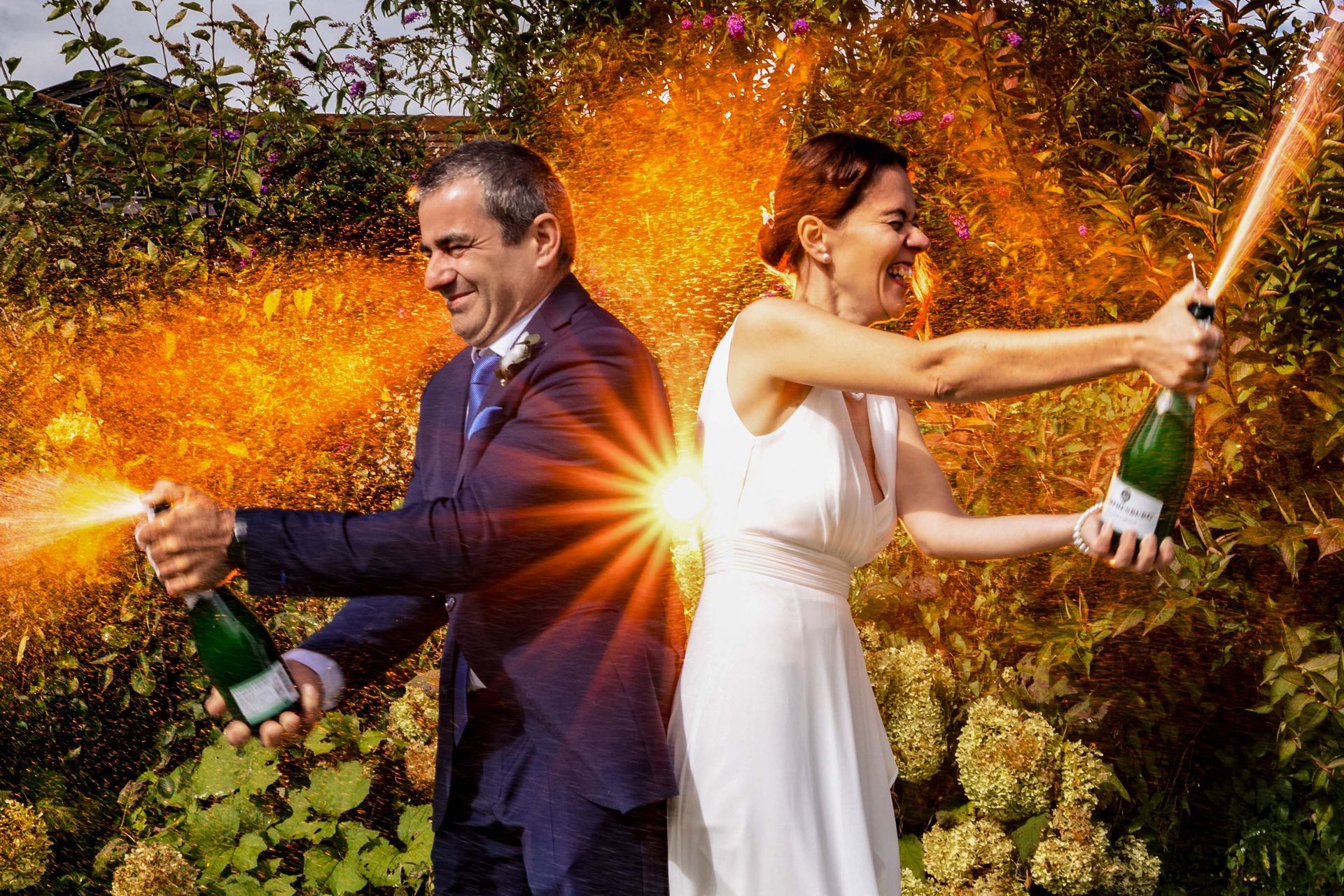 Brautpaar spritzt ausgelassen mit Sektflaschen bei einer Fraueninsel-Hochzeit am Chiemsee.
