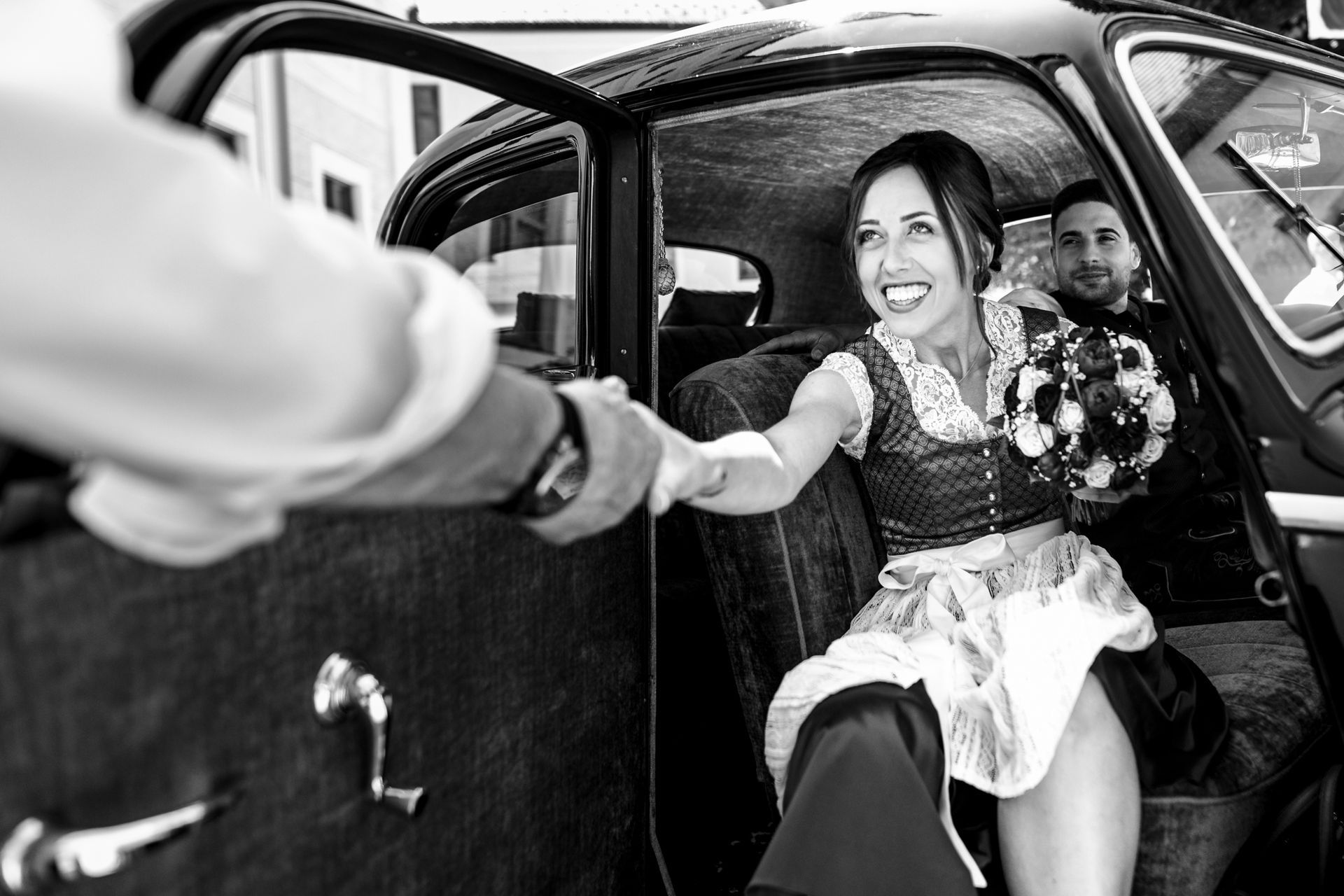 braut in dirndl reicht einem mann die hand zum aussteigen aus dem brautauto