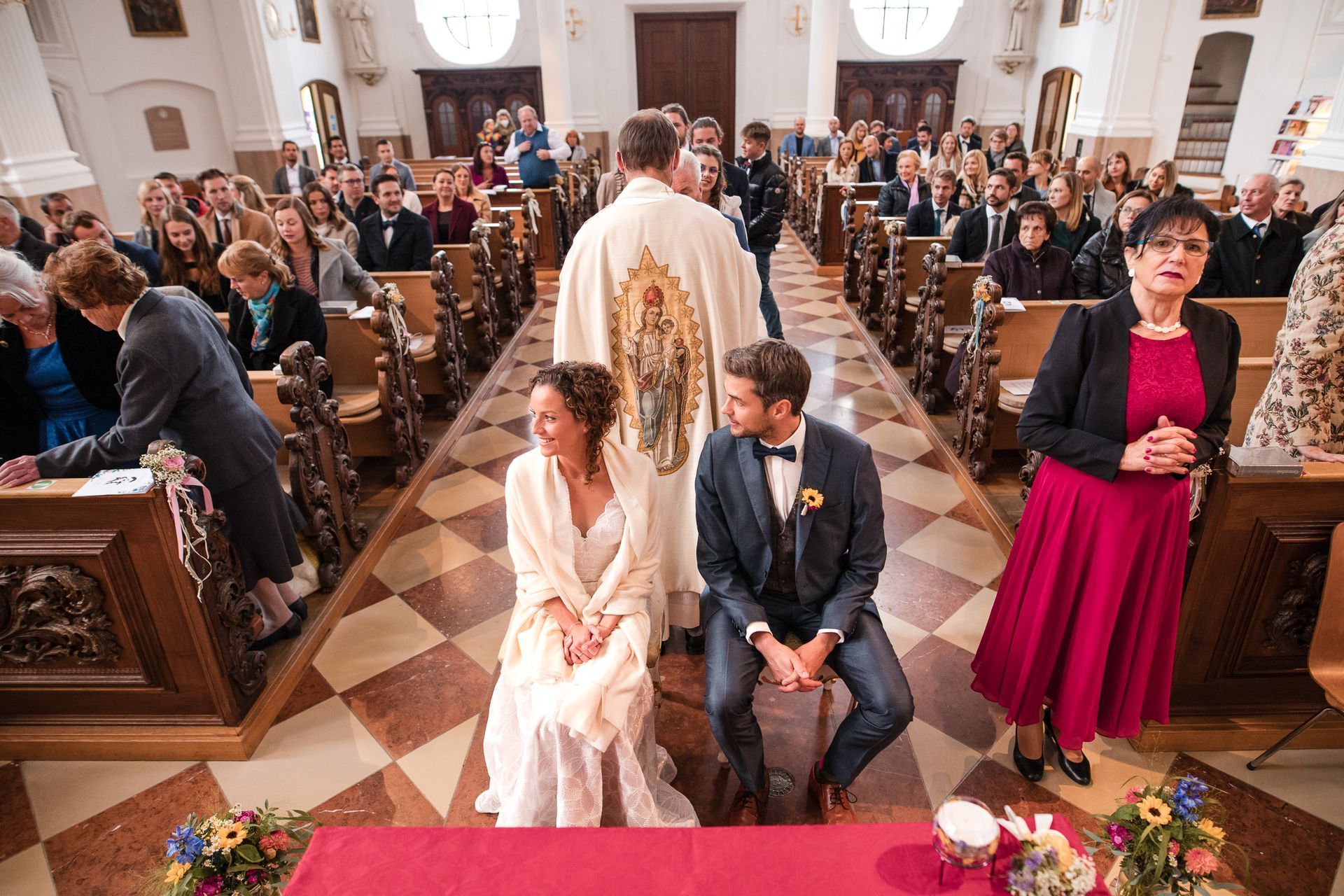 brautpaar sitzt in kiche bei hochzeit der pfarrer steht hinter ihnen mit dem rücken zum brautpaar