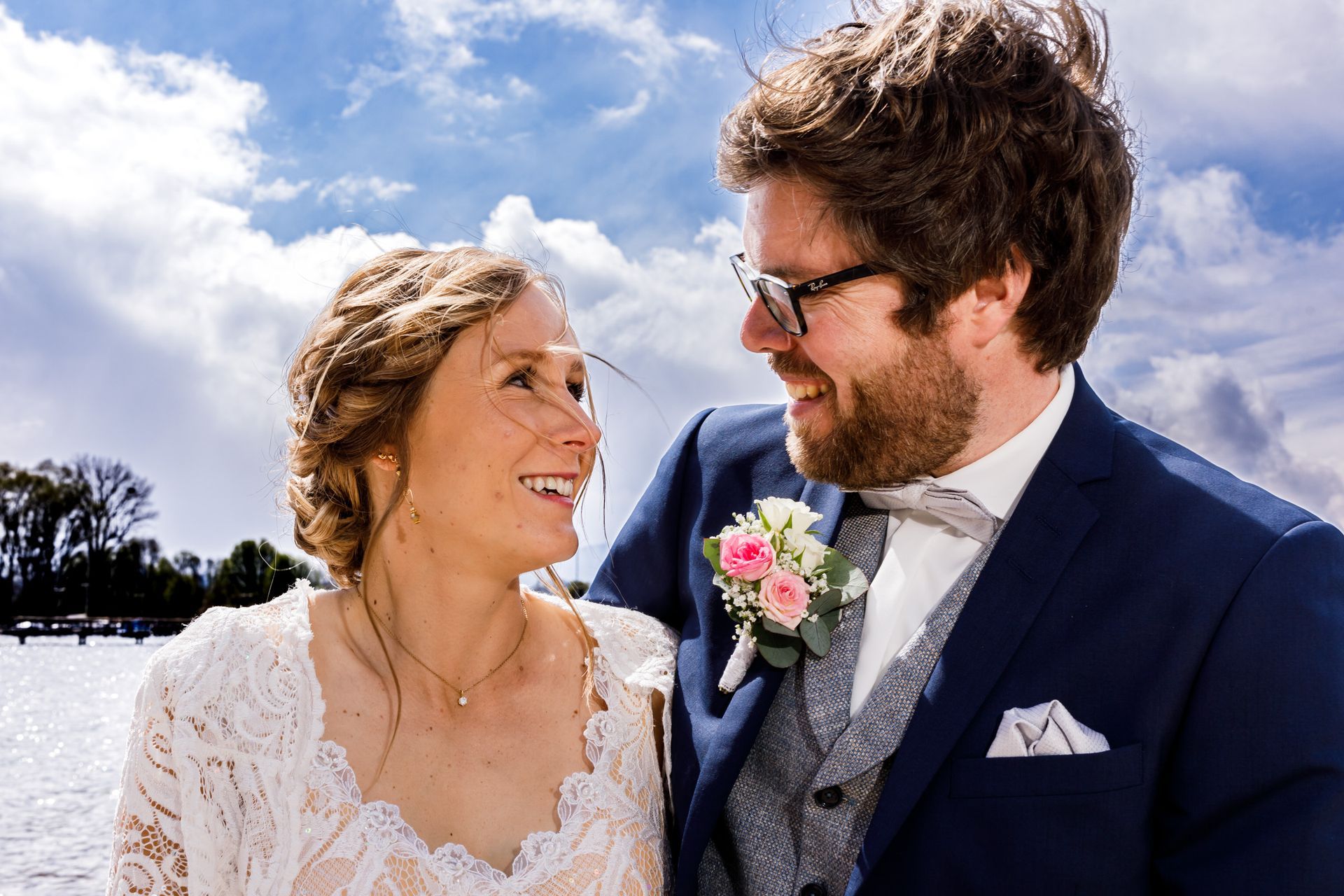 strandbad uebersee chiemsee hochzeitsfotograf andrea kuehl brautpaar lacht vor wolkenhimmel
