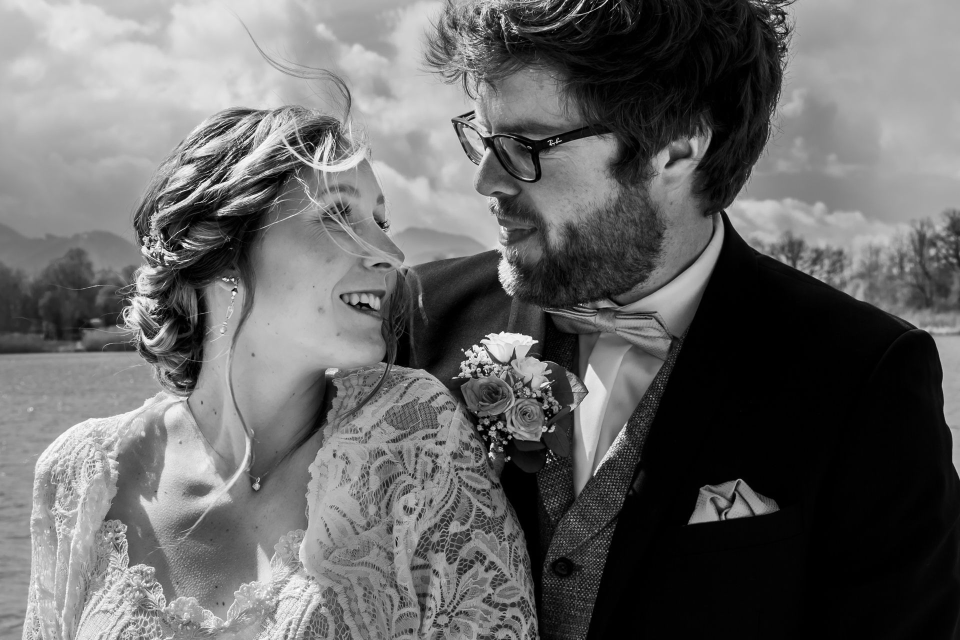 strandbad uebersee chiemsee hochzeitsfotograf andrea kühl brautpaar lacht vor wolkenhimmel schwarz weiß