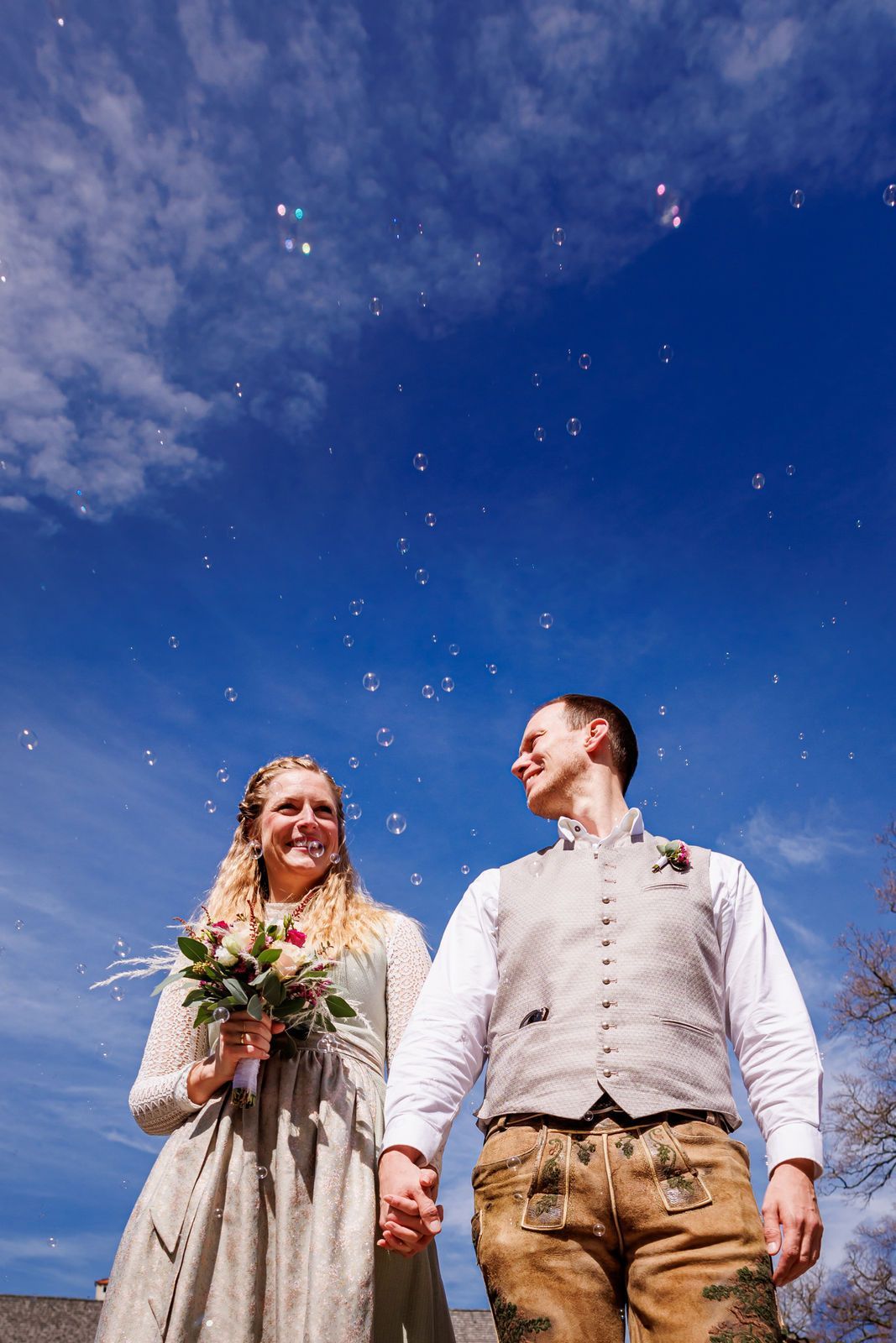 hochzeitspaar in tracht mit seifenblasen vor blauem himmel bei schönem wetter auf der fraueninsel im chiemsee