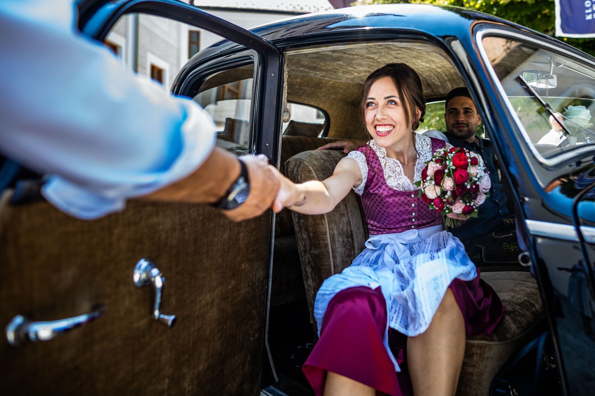 braut in dirndl reicht einem mann die hand zum aussteigen aus dem brautauto