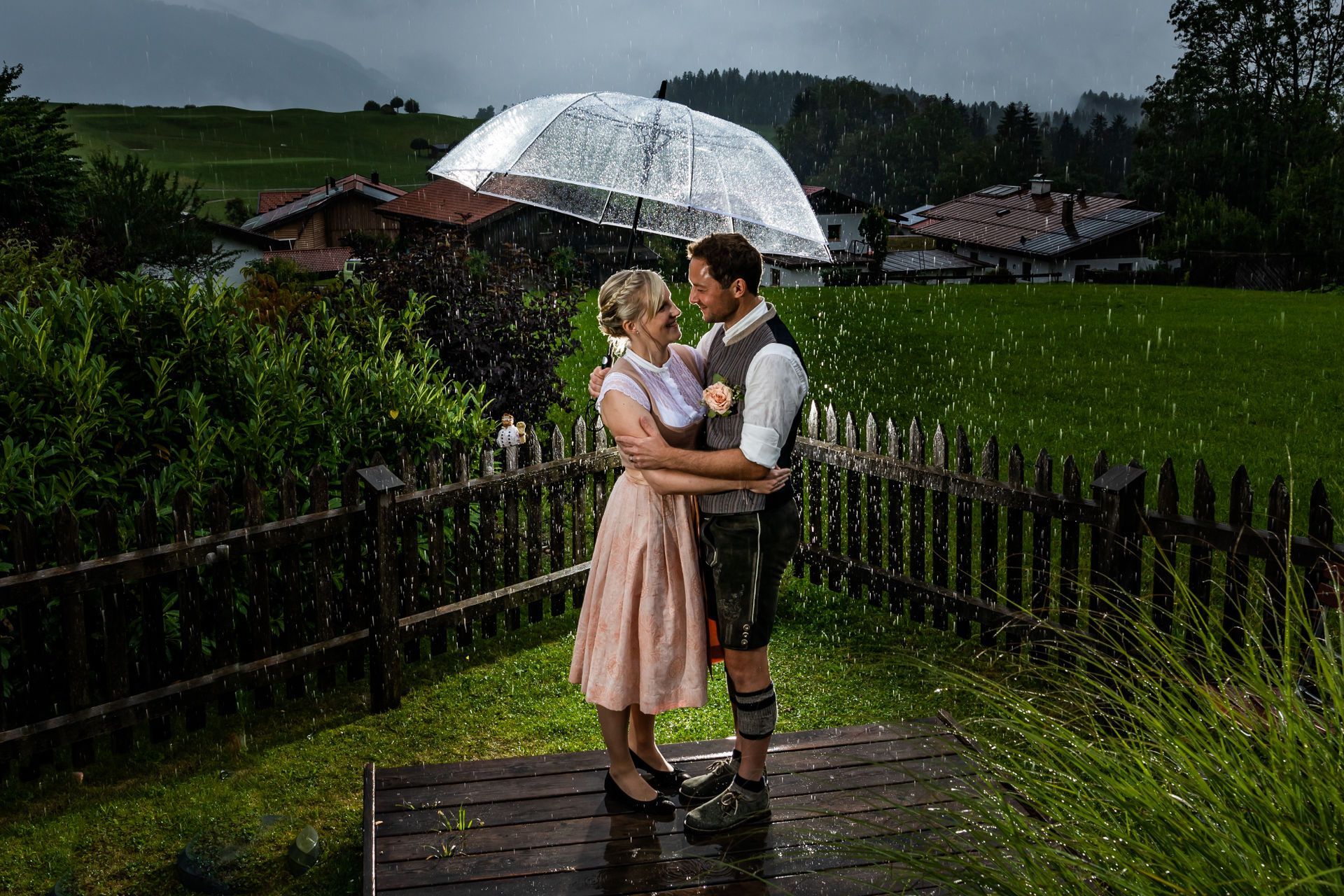 brautpaar in tracht im Regen in chieming unter transparentem schirm