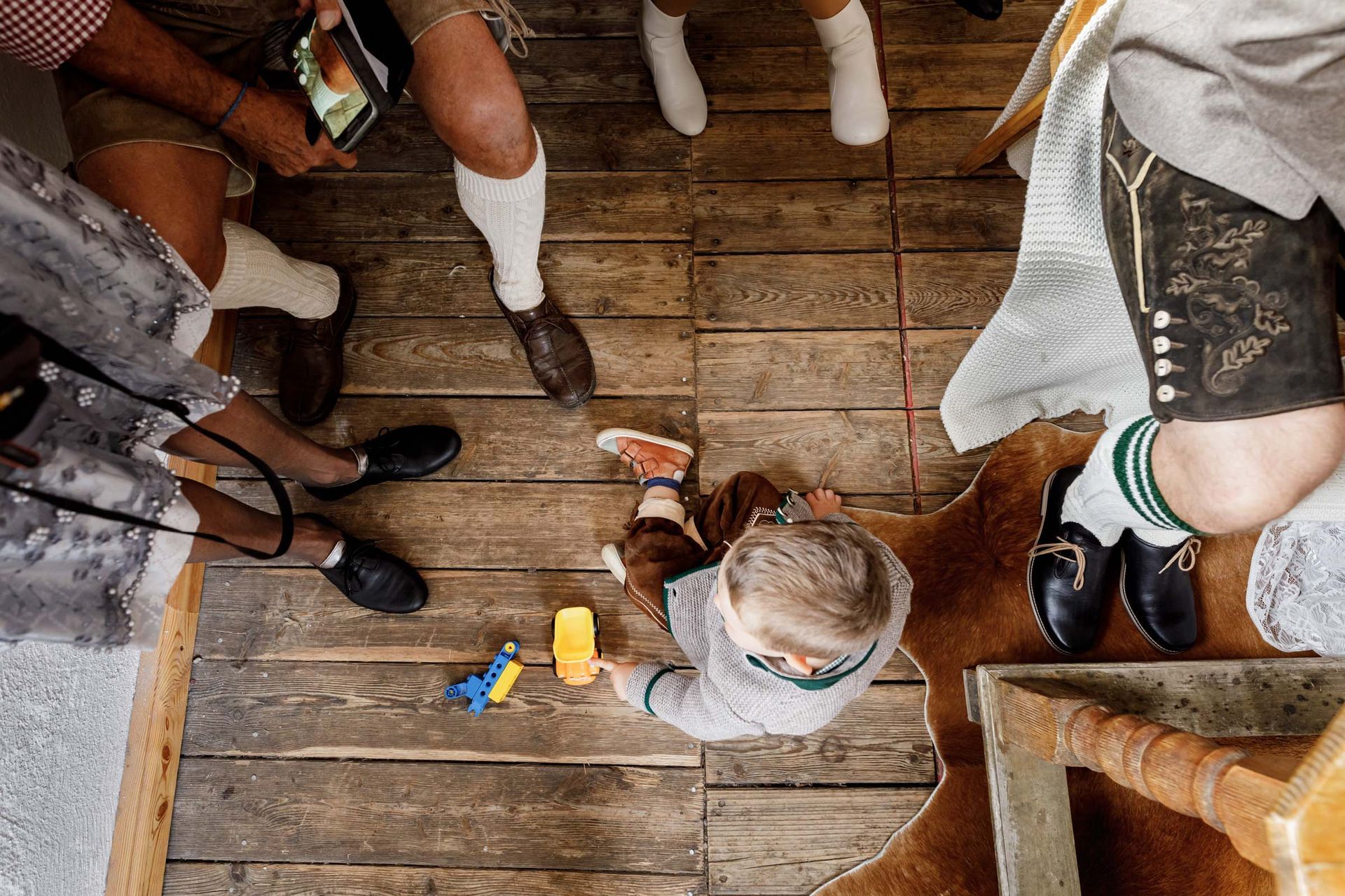 hochzeitsfotograf schliersee almbad huberspitz kind sitzt mit spielzeug auf dem boden sicht von oben auf das kind