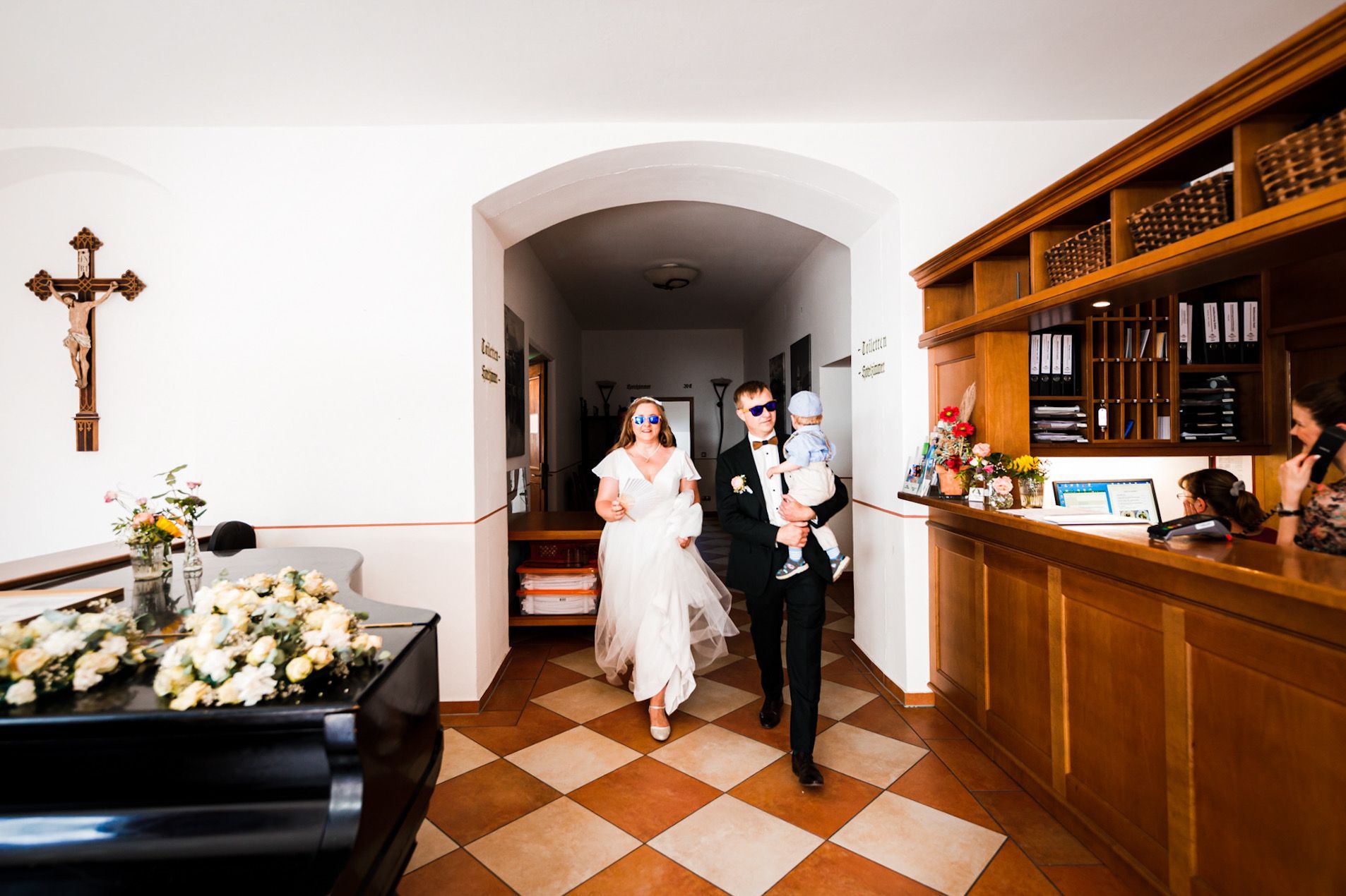 hochzeitspaar im mafiastyle und sonnenbrille auf der nase laufen im flur dem hochzeitsfotografen entgegen