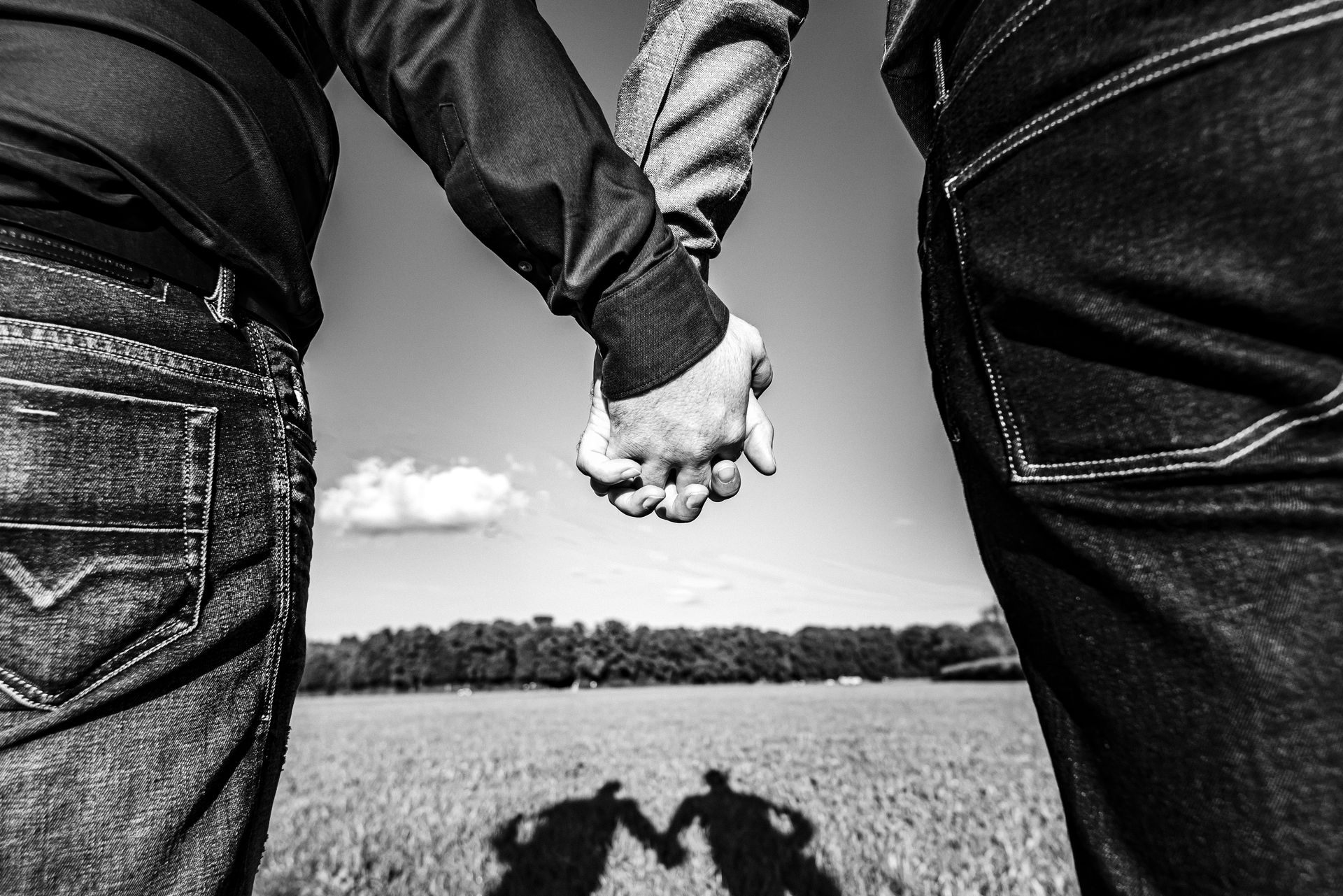 schwules paar hält sich an der hand und ihr schatten bildet sich auf dem boden ab fotografiert in der natur