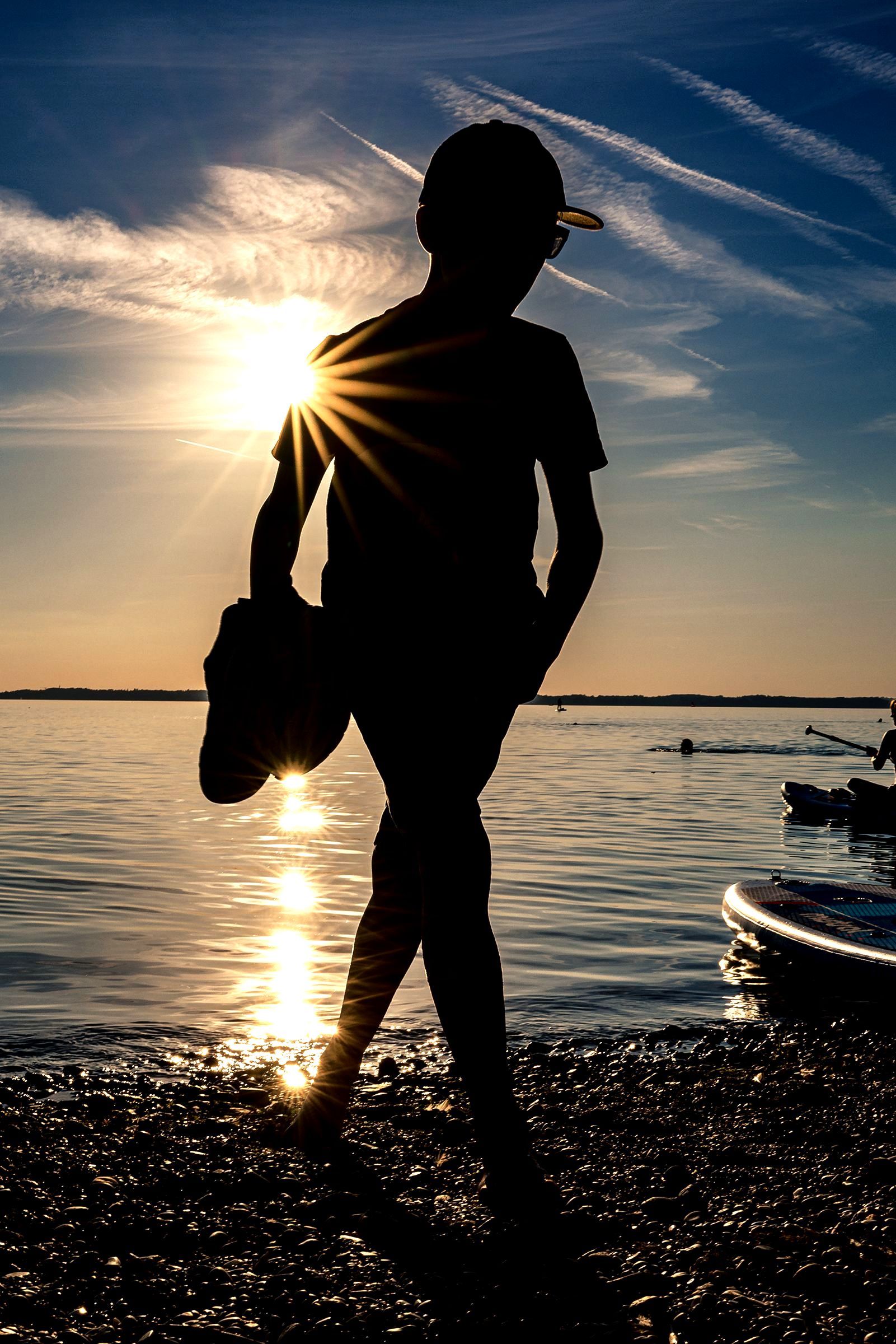 Silhouette am Chiemsee silhouette eines jungen mit schuhen in der hand am chiemsee