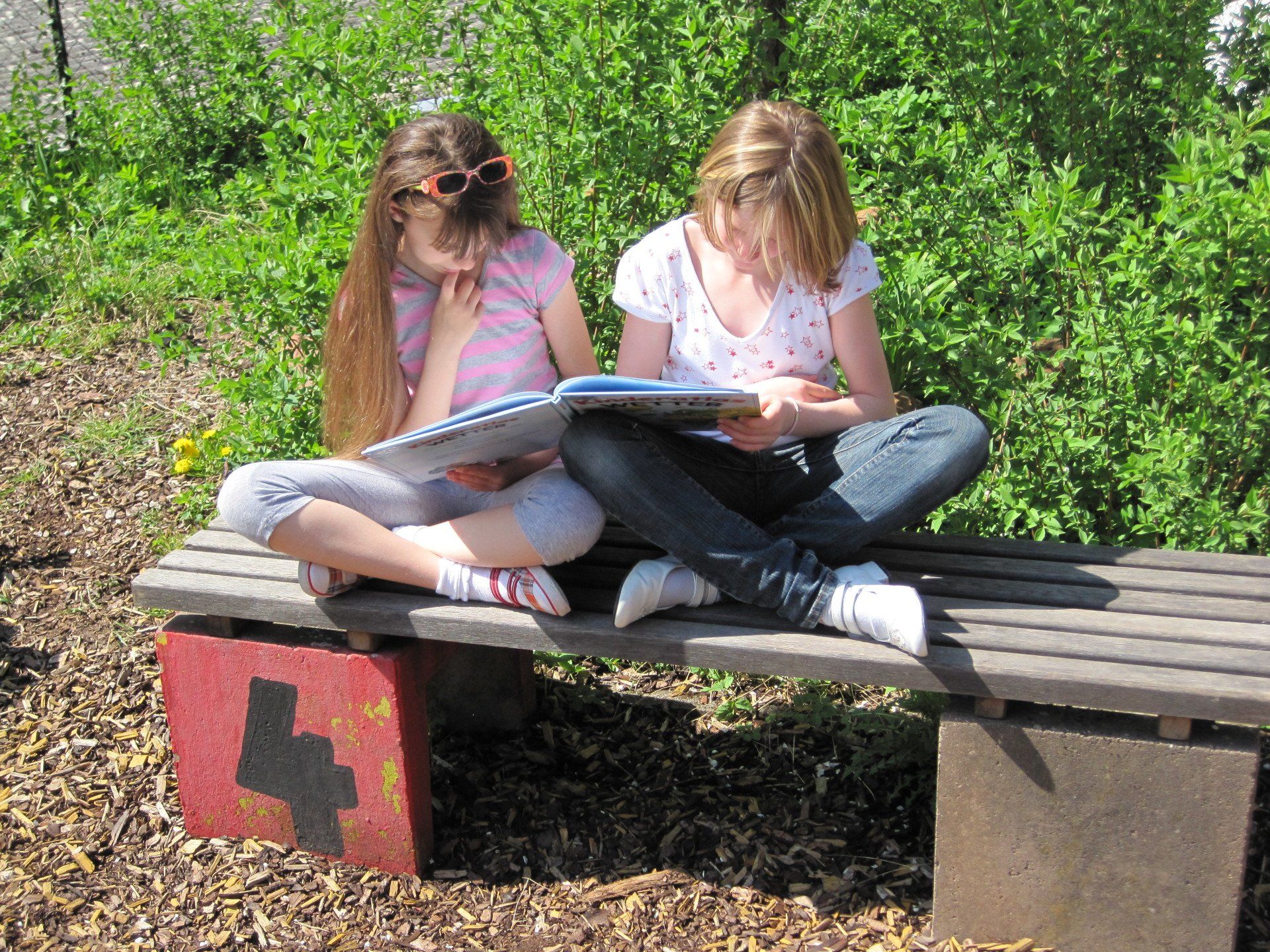 Zwei Mädchen sitzen auf Bank und lesen