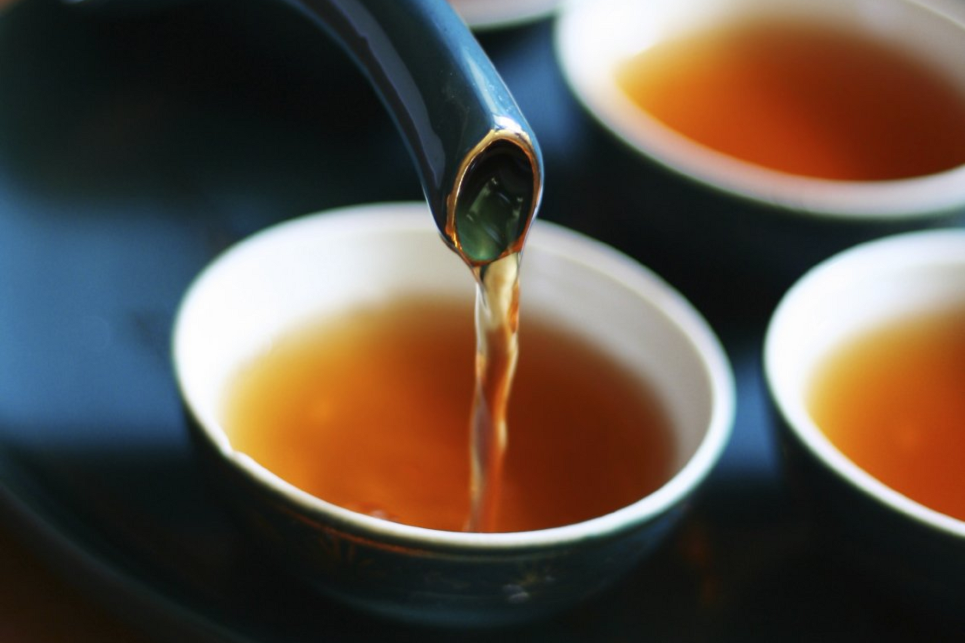 Porzellantassen und Kannenausguss, aus dem Tee fließt