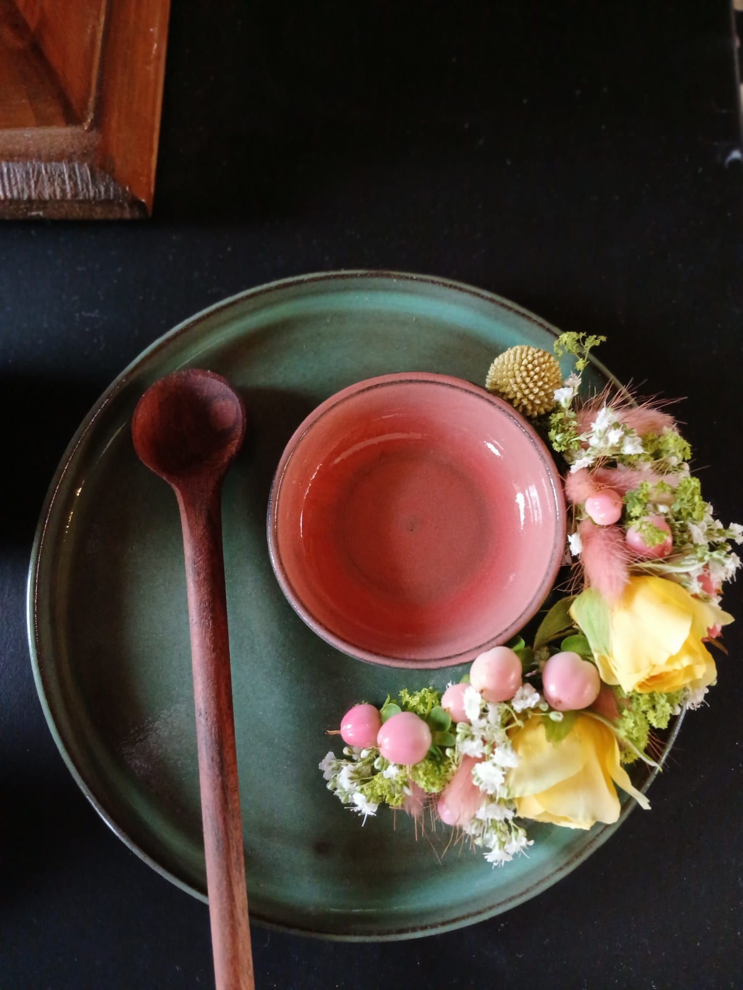 grüner Keramikteller mit rosa Schale und Löffel sowie Blumenkranz - Farbpsychologie Natürlichkeit