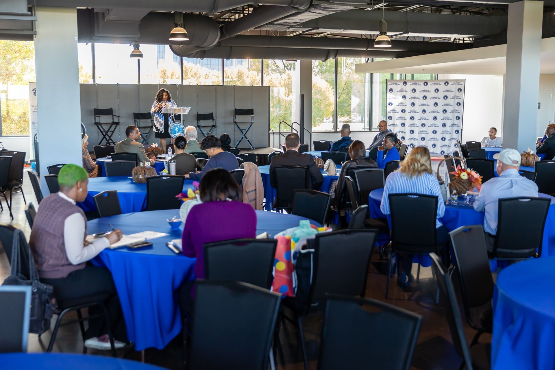 Attendees at a networking venent seated at tables listening to a speaker.