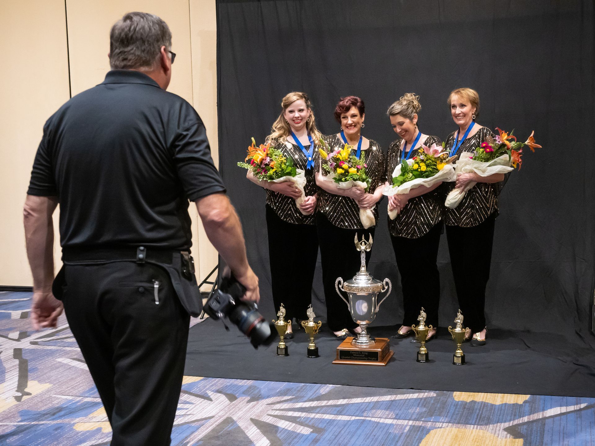 A photographer dressed in black preparing to take a group photo of award recipients.