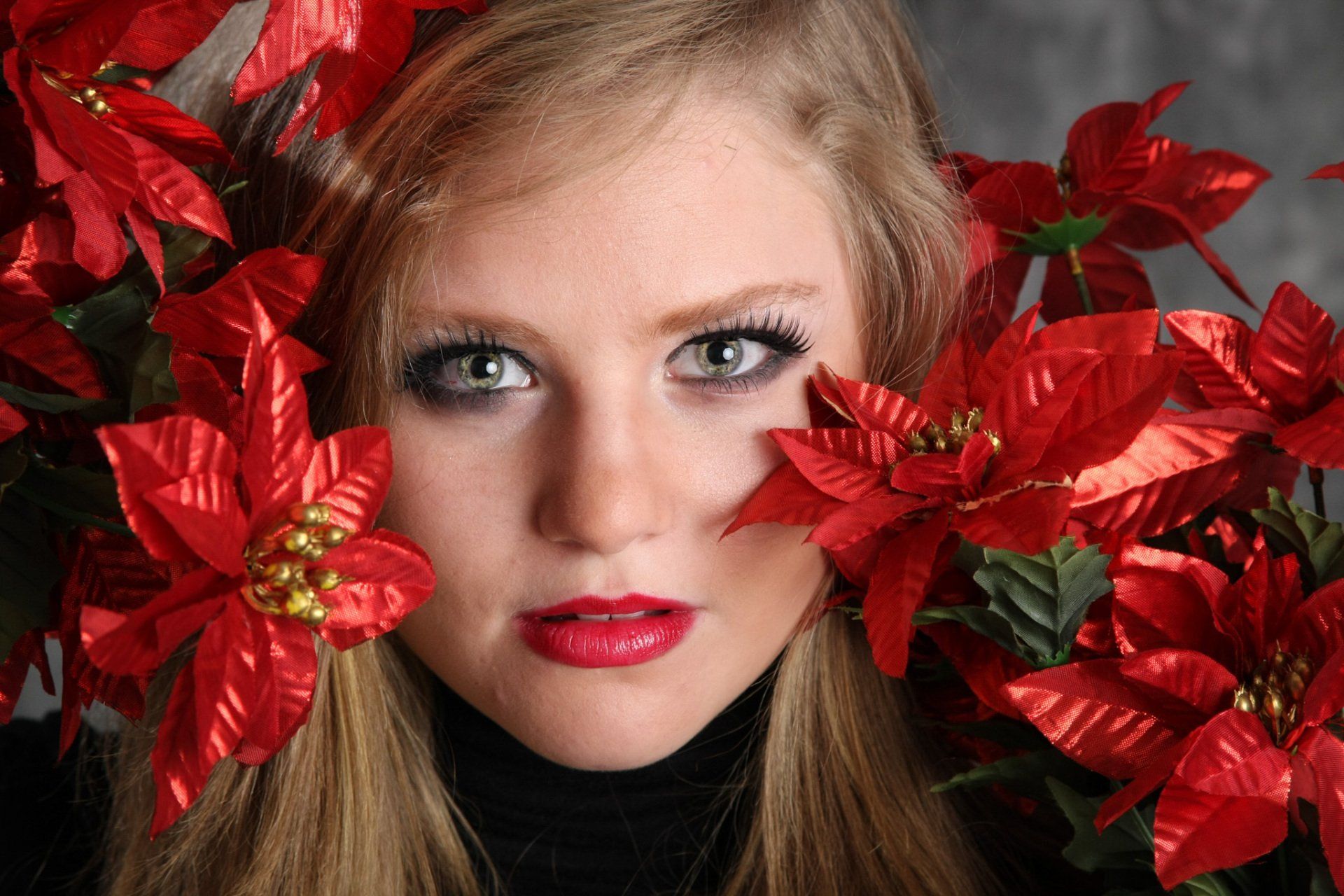 A woman with blond hair holding red flowers around her face for a creative studio portrait