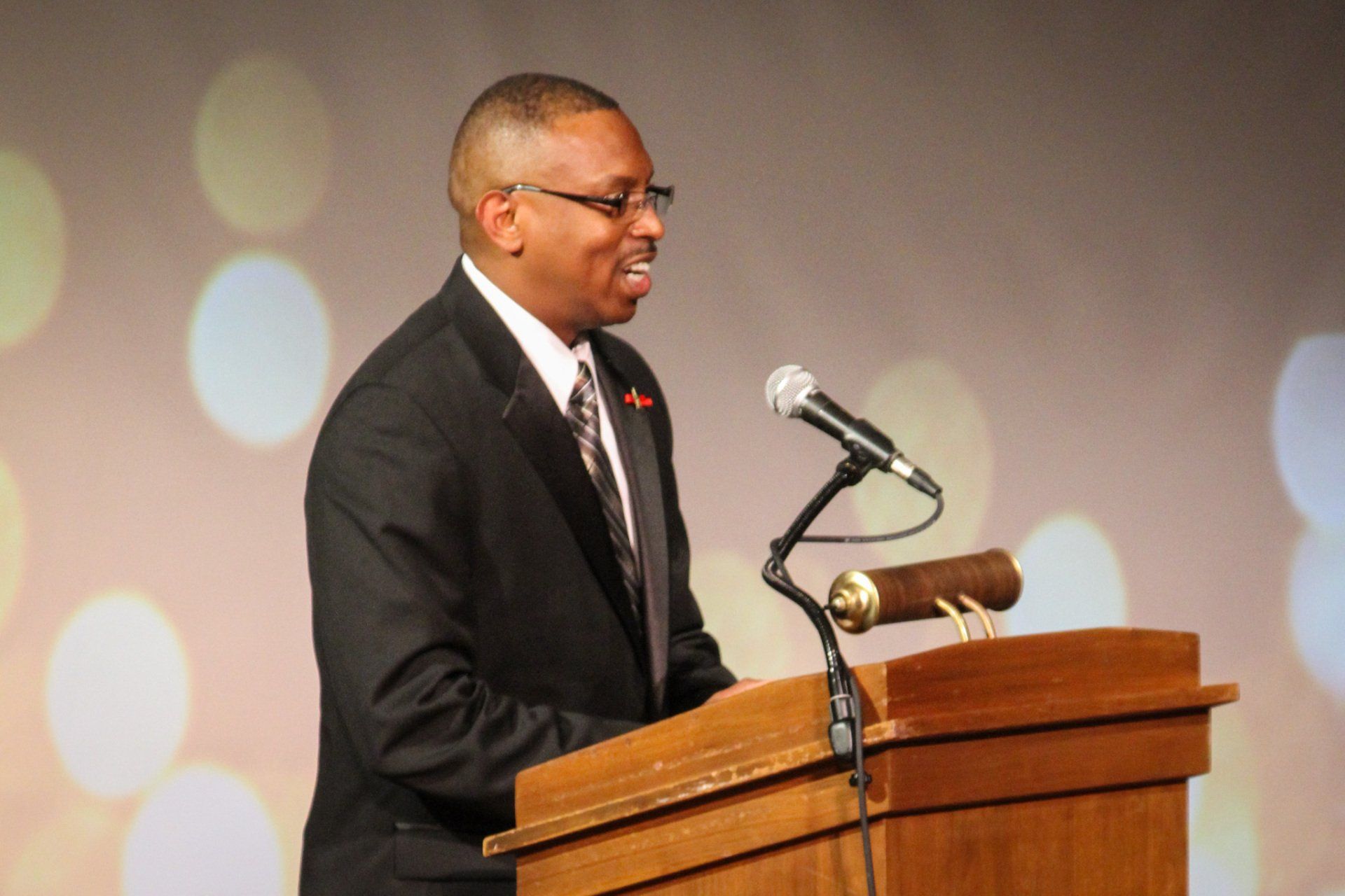 A man in a suit standing in front of a podium and microphone speaking.