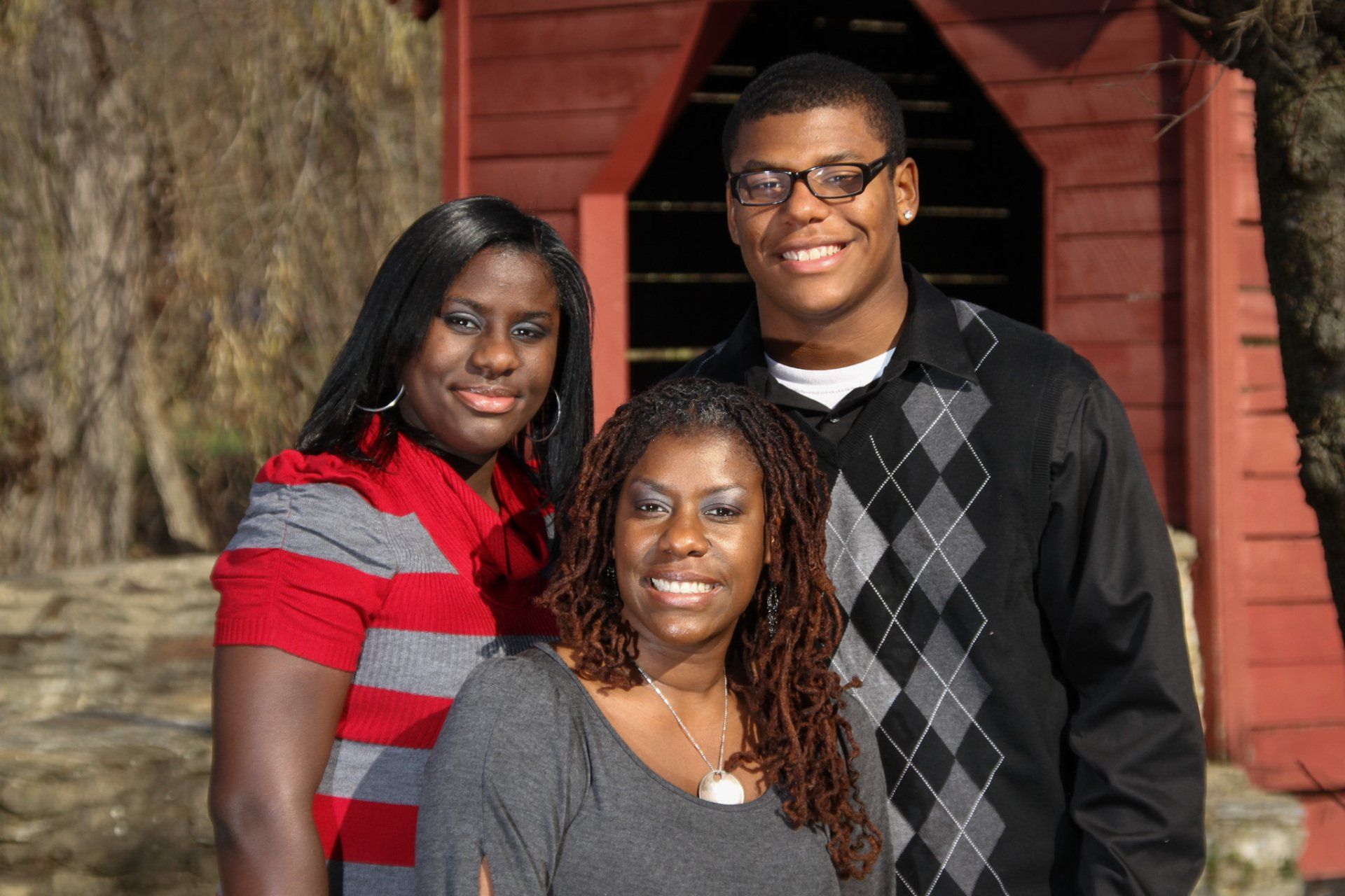 A family of three posing in front of the red covered bridge at Baker Park for family portraits.