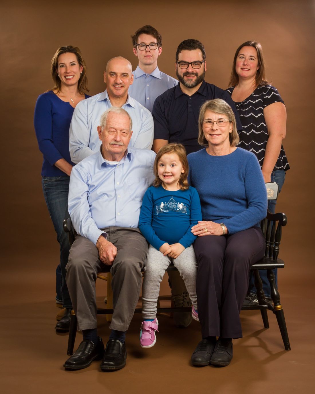 A studio portrait of a large family, grandparents, parents and children with a brown background