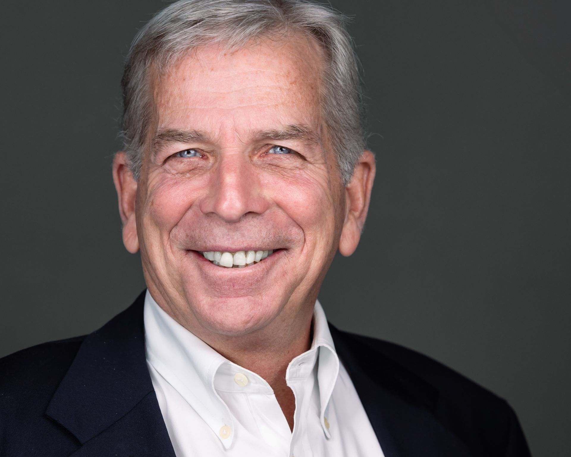 A headshot of a businessman in a black suit jacket and white button up shirt.