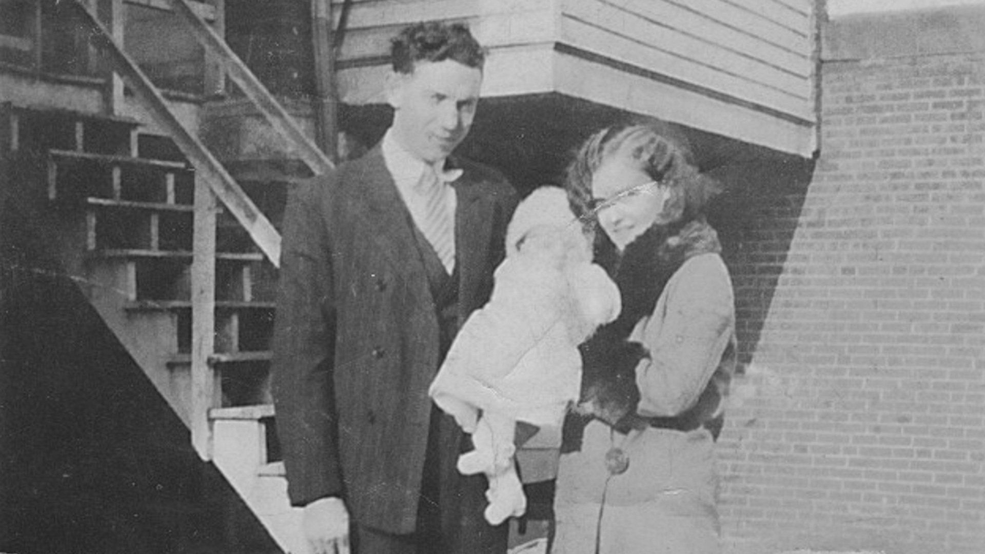 An old, damaged black and white photograph of a couple holding their infant child.