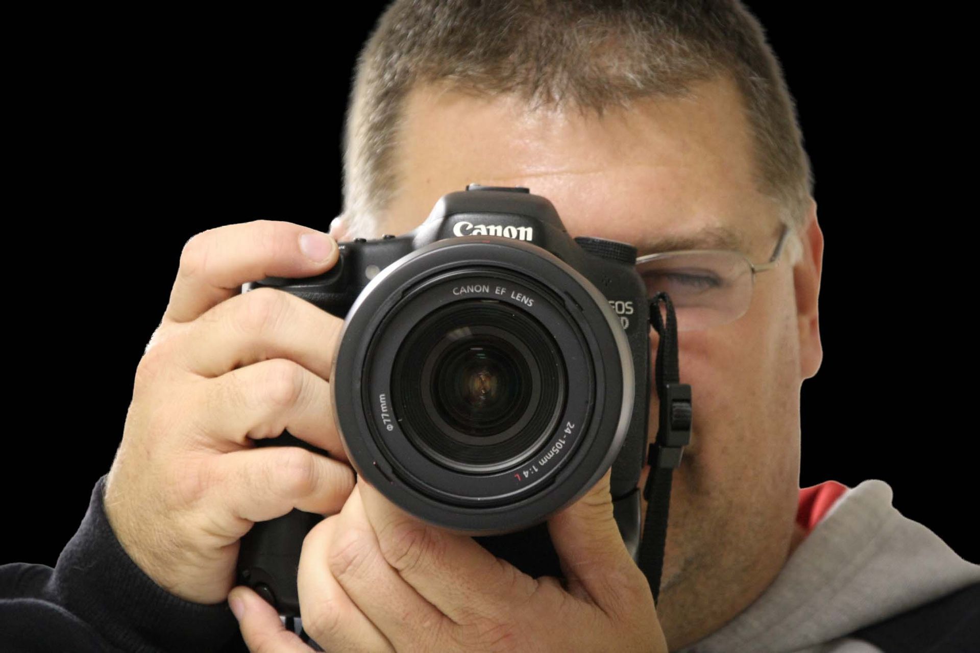 A man holding a professional camera pointing it at the viewer preparing to take a picture.