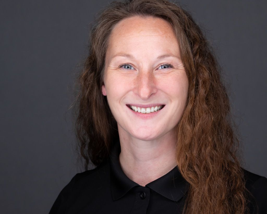 A headshot of woman with frizzy brown hair in a black polo shirt