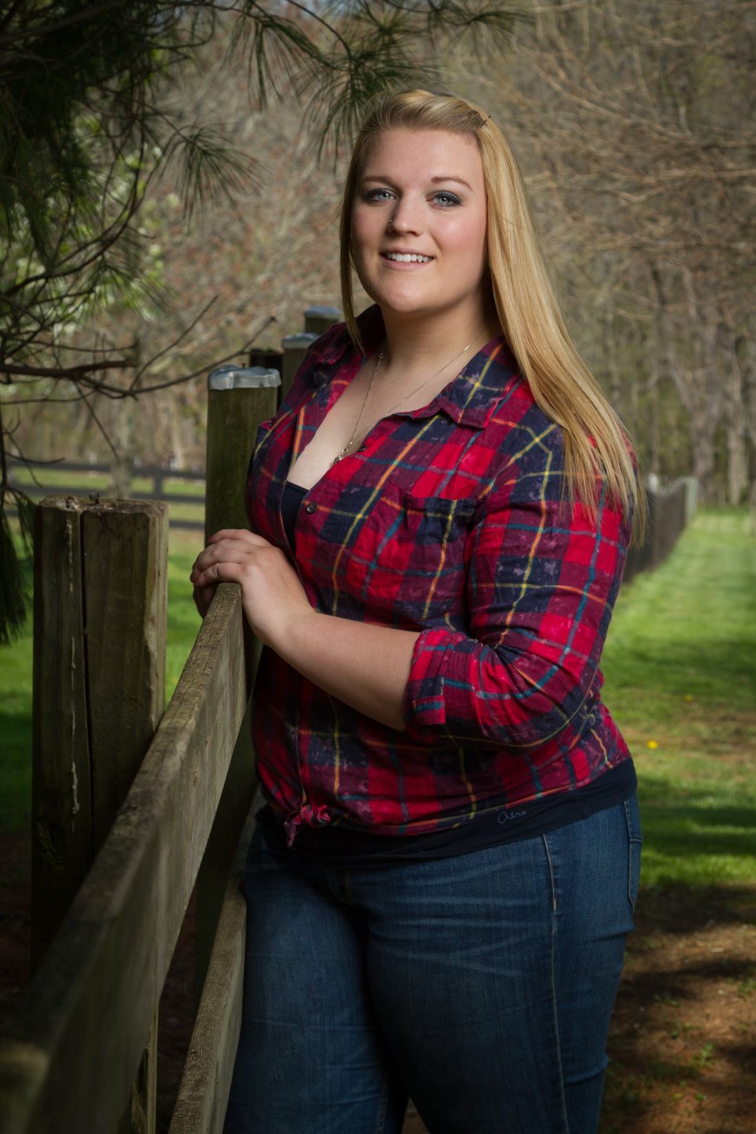An outdoor senior portrait of a girl in a red plaid standing along a wooden fence