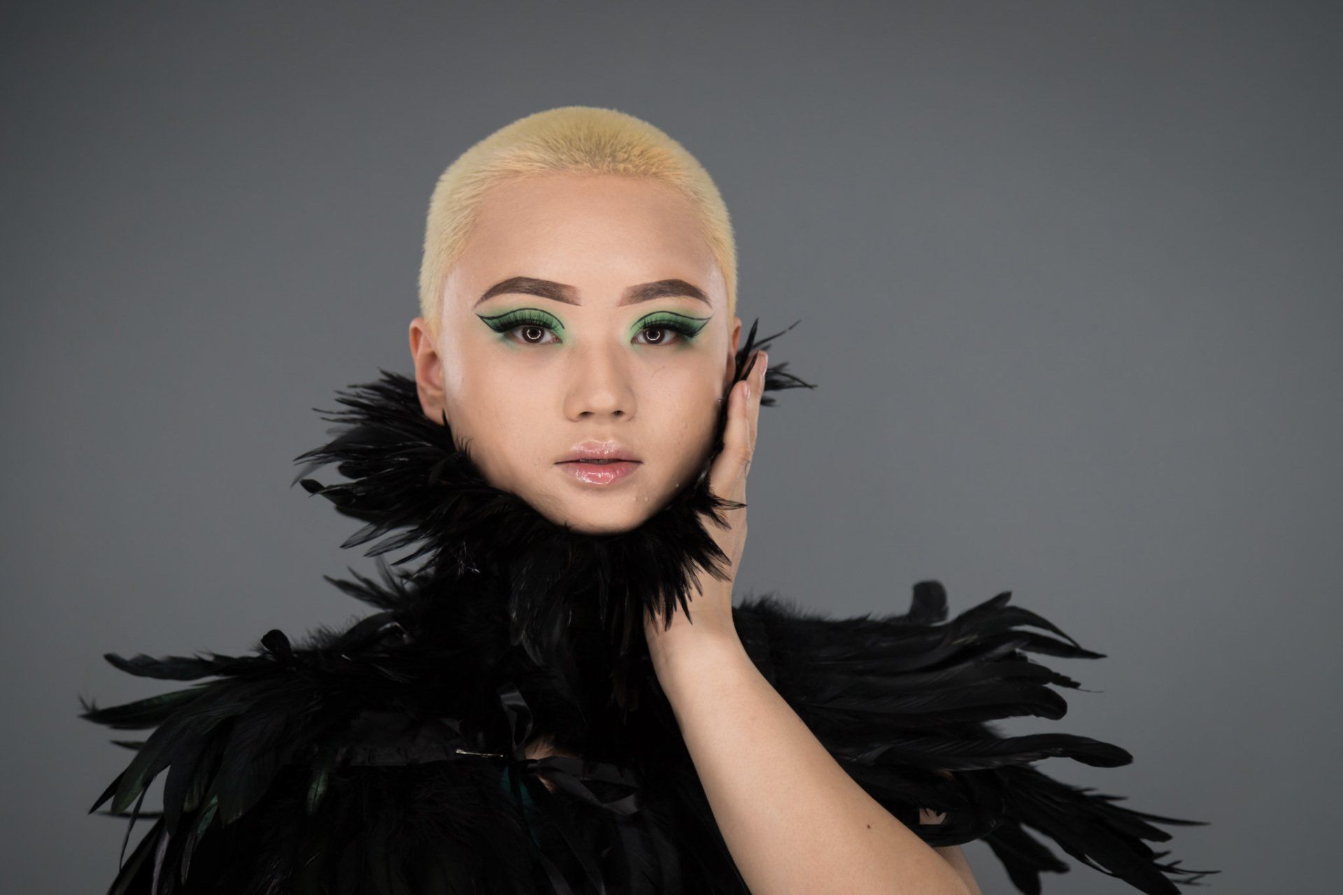A female model with short cut blond hair in a black dress and black feather boa.