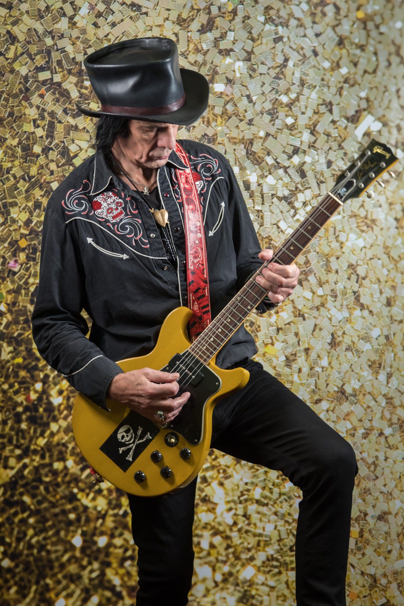 A portrait of a rock guitarist in a black leather top hat playing his guitar against a glittery background