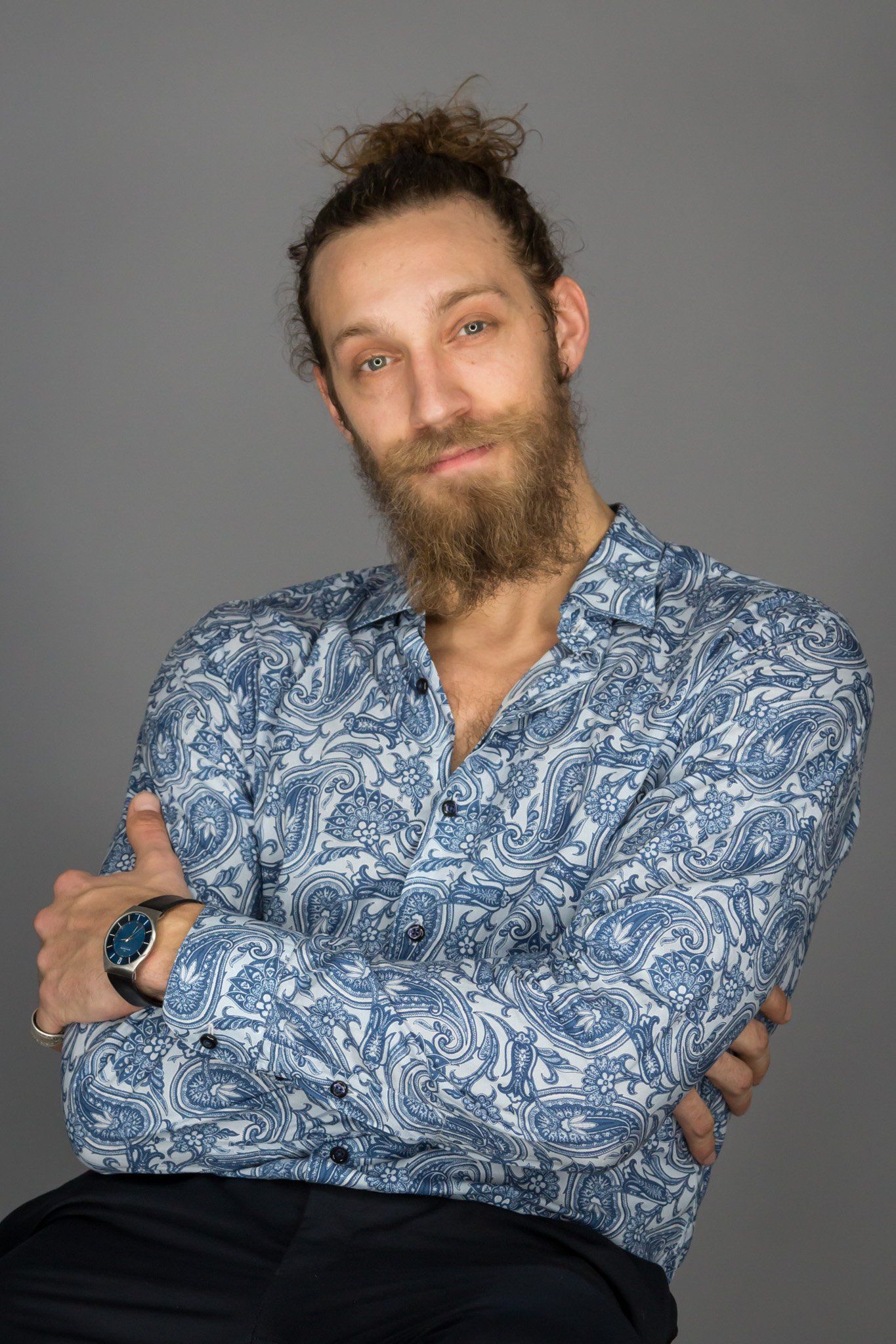 A man with scruffy brown hair and a beard wearing a blue and white paisley shirt.