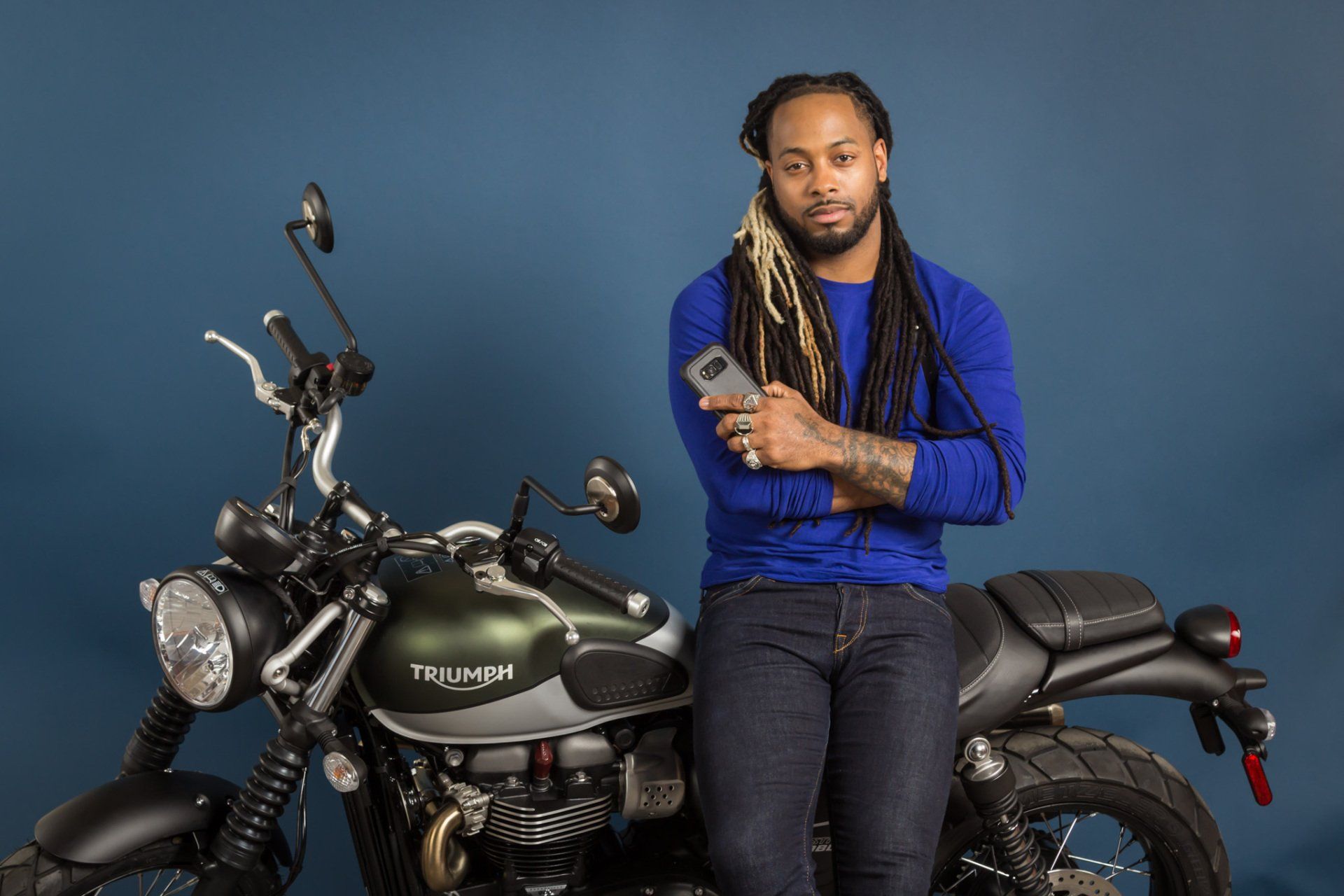 A model posing with a cell phone and a green Triumph motorcycle.