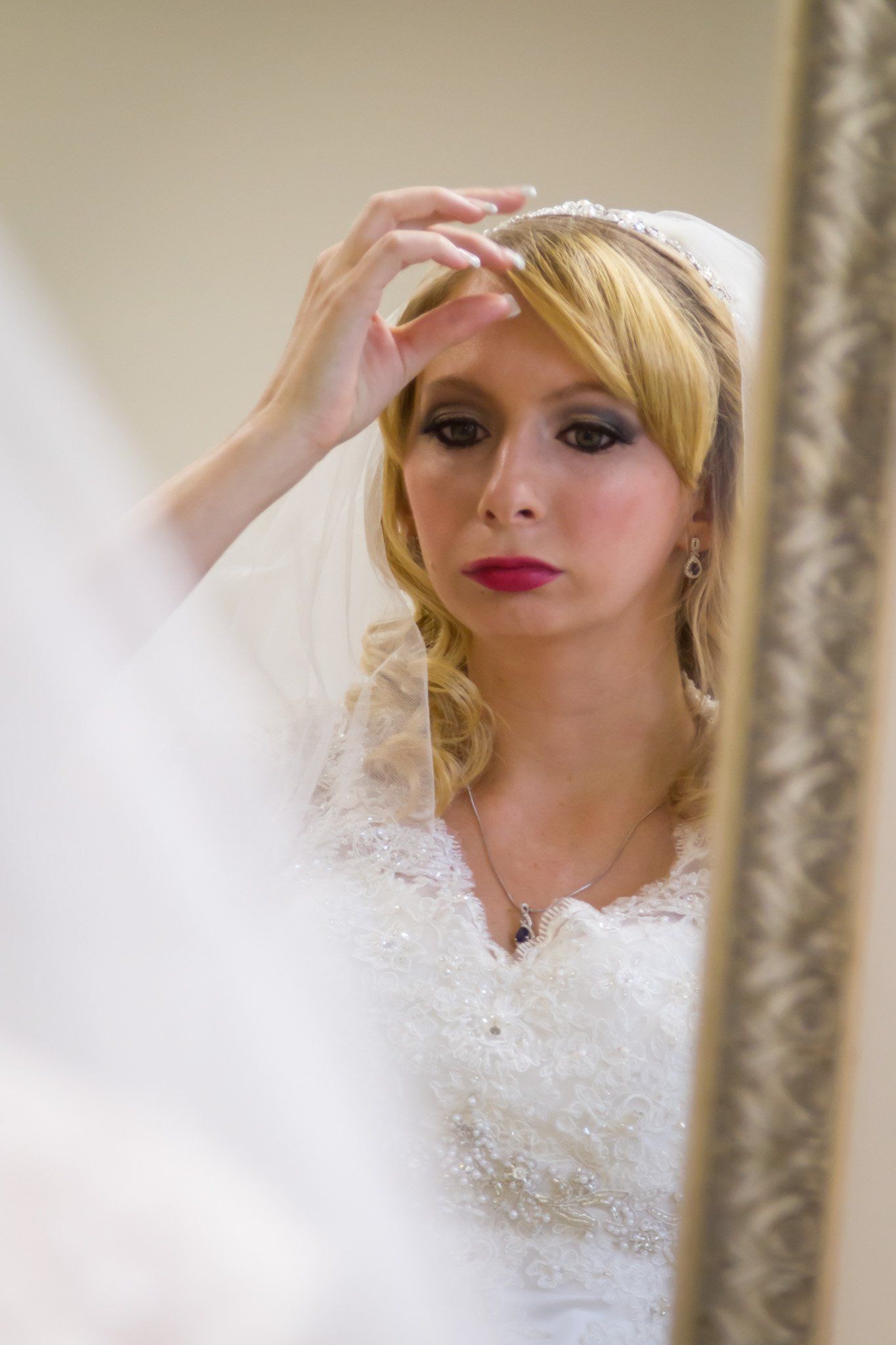 A portrait of the bride looking at herself in the mirror as she gets ready and checks her veil