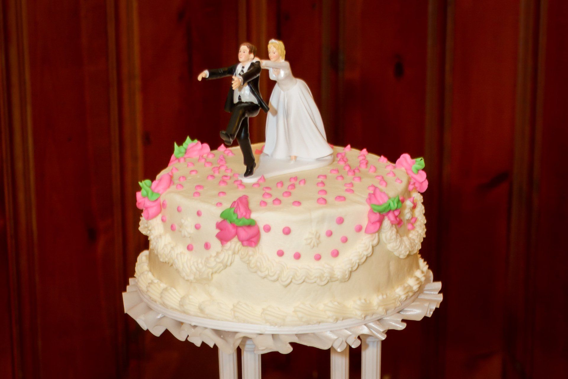 A picture of the comical wedding cake top showing a groom running away and a bride grabbing him by the collar