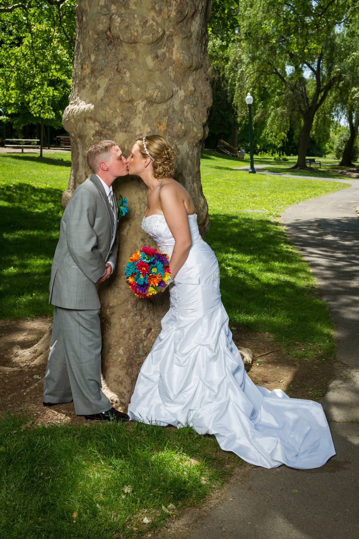 An outdoor portrait of a newly married couple kissing in front of a large tree
