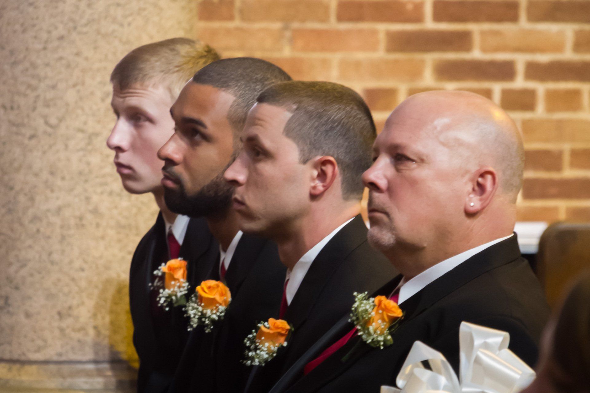 A side view of all the groomsmen seated in a line on a pew in their black tuxedos